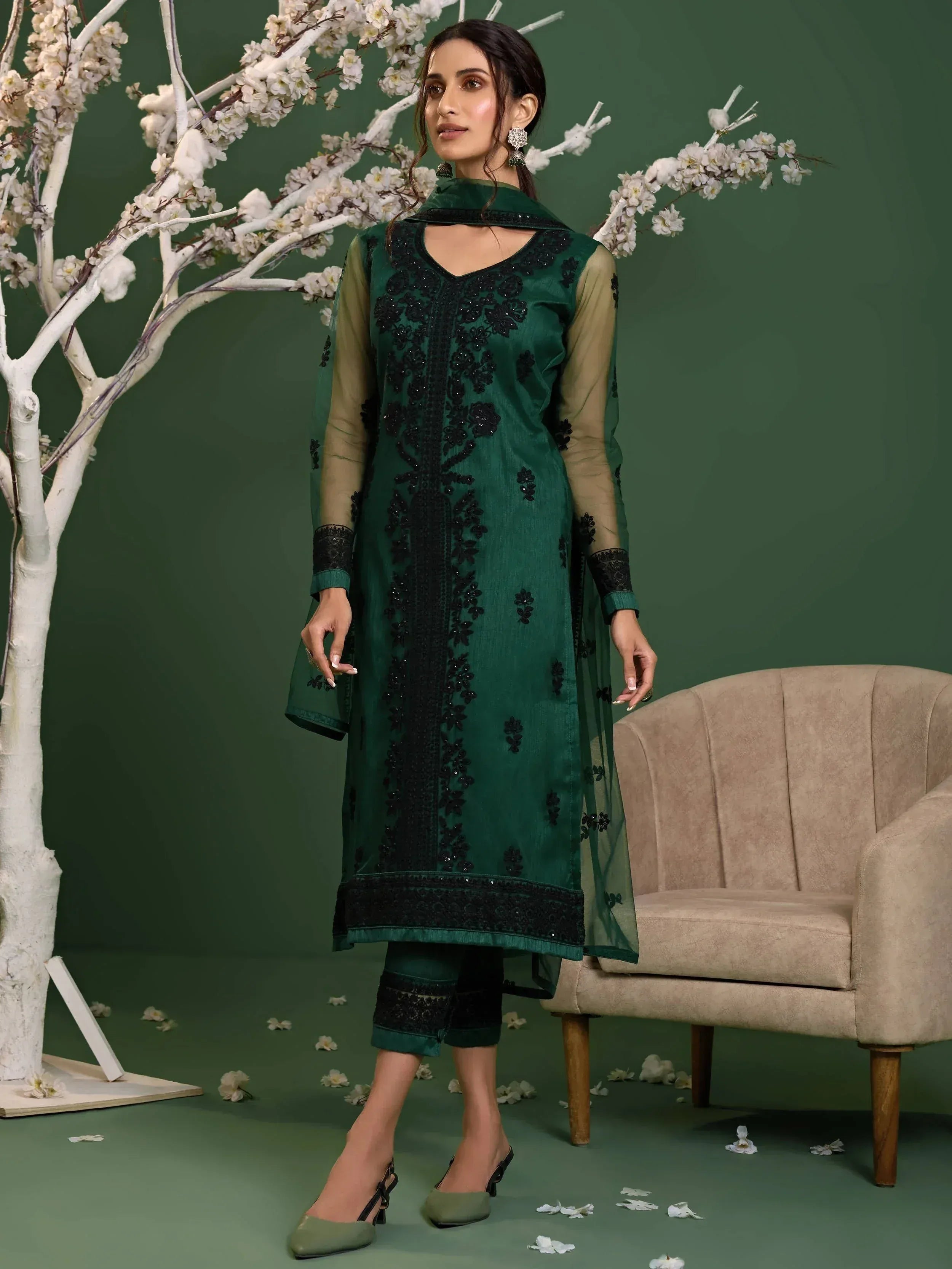 Emerald green embroidered salwar kameez with sheer sleeves and black detailing, styled with floral backdrop