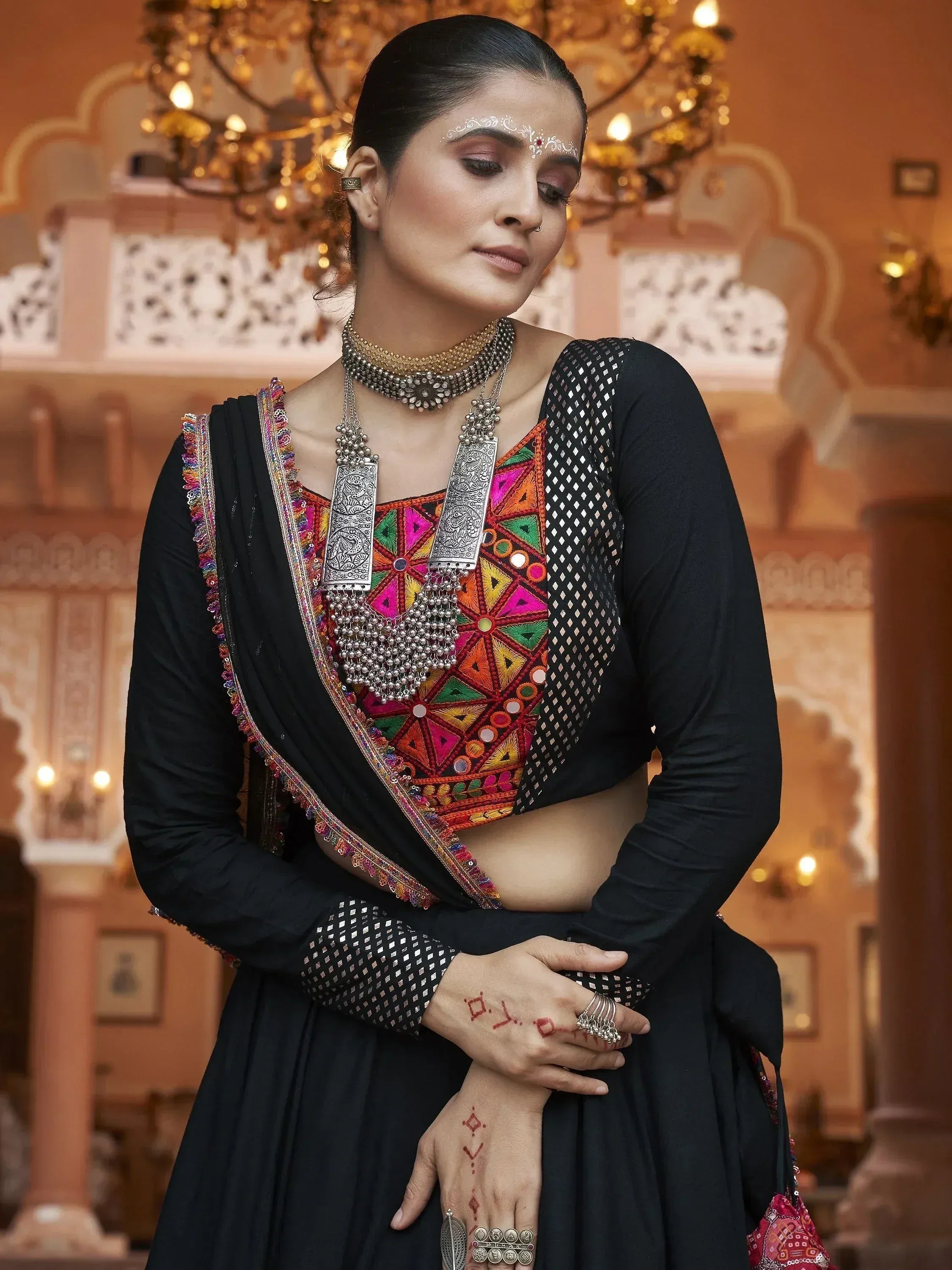 Black ethnic wear with colorful mirror work, silver jewelry, and traditional henna designs for Indian festive occasions.