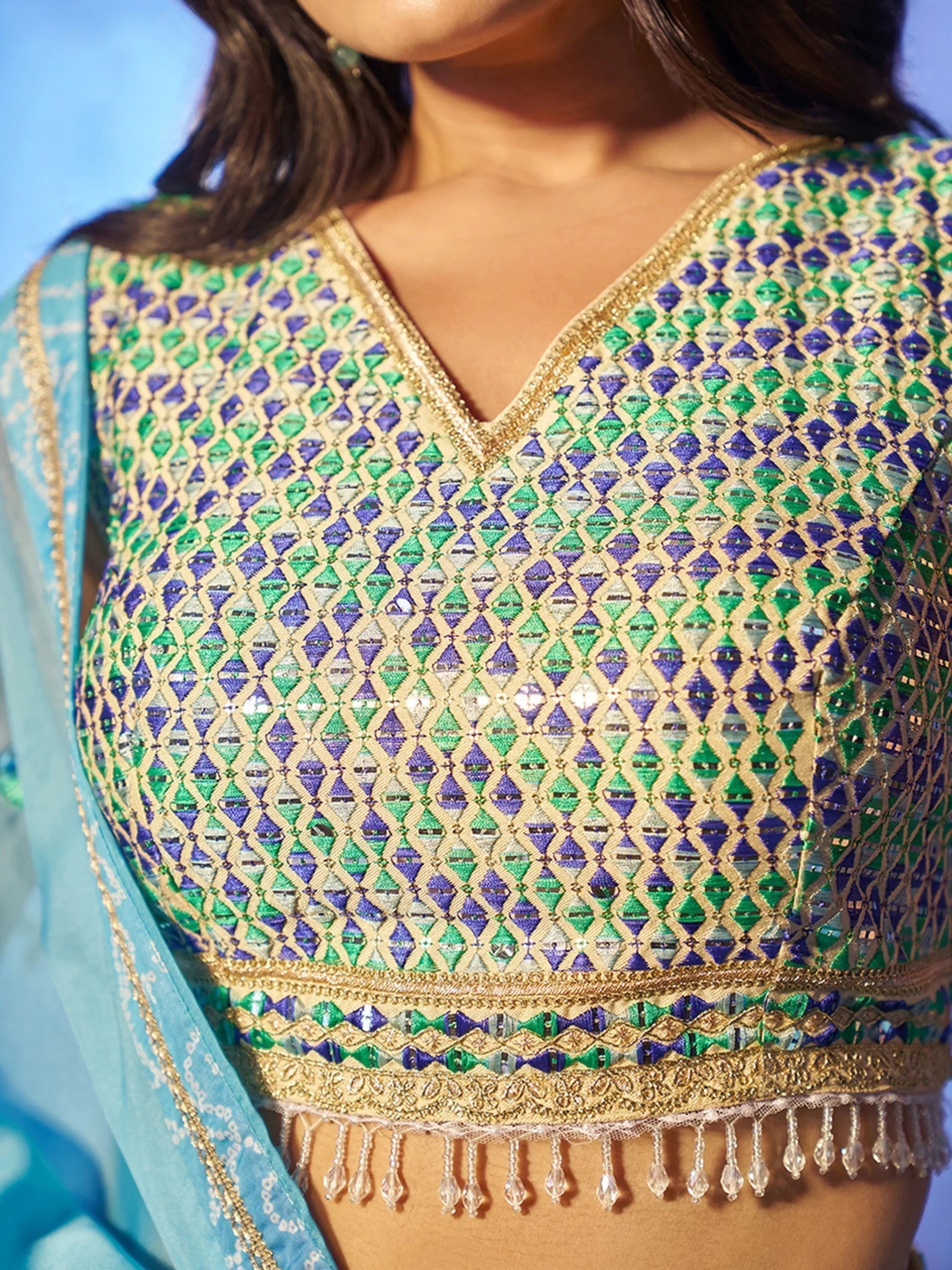 Green and blue embroidered ethnic blouse with gold trim and crystal tassels, paired with light blue dupatta.