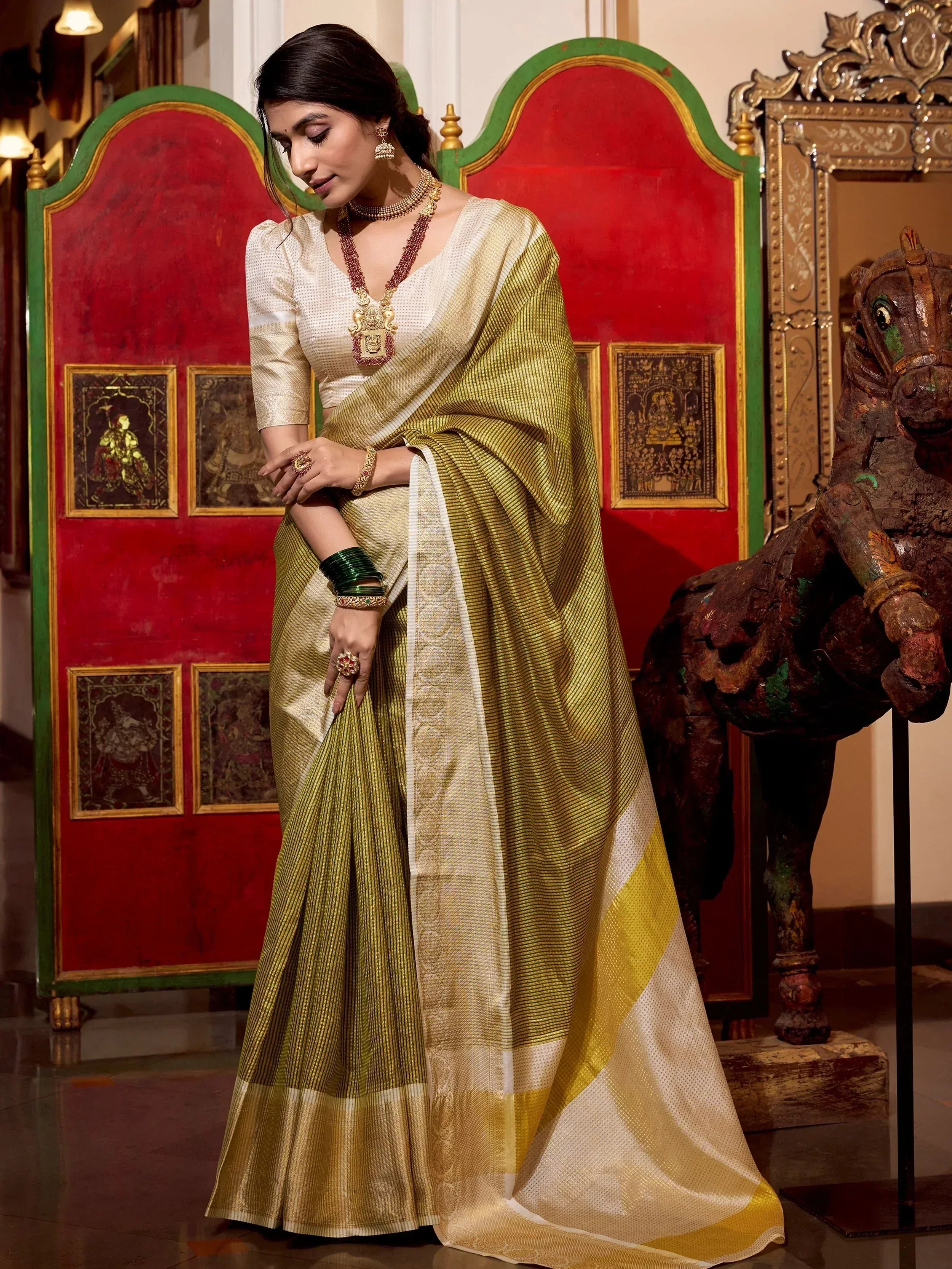 Elegant woman in traditional Indian saree with gold and green stripes, styled with temple jewelry for festive occasions.