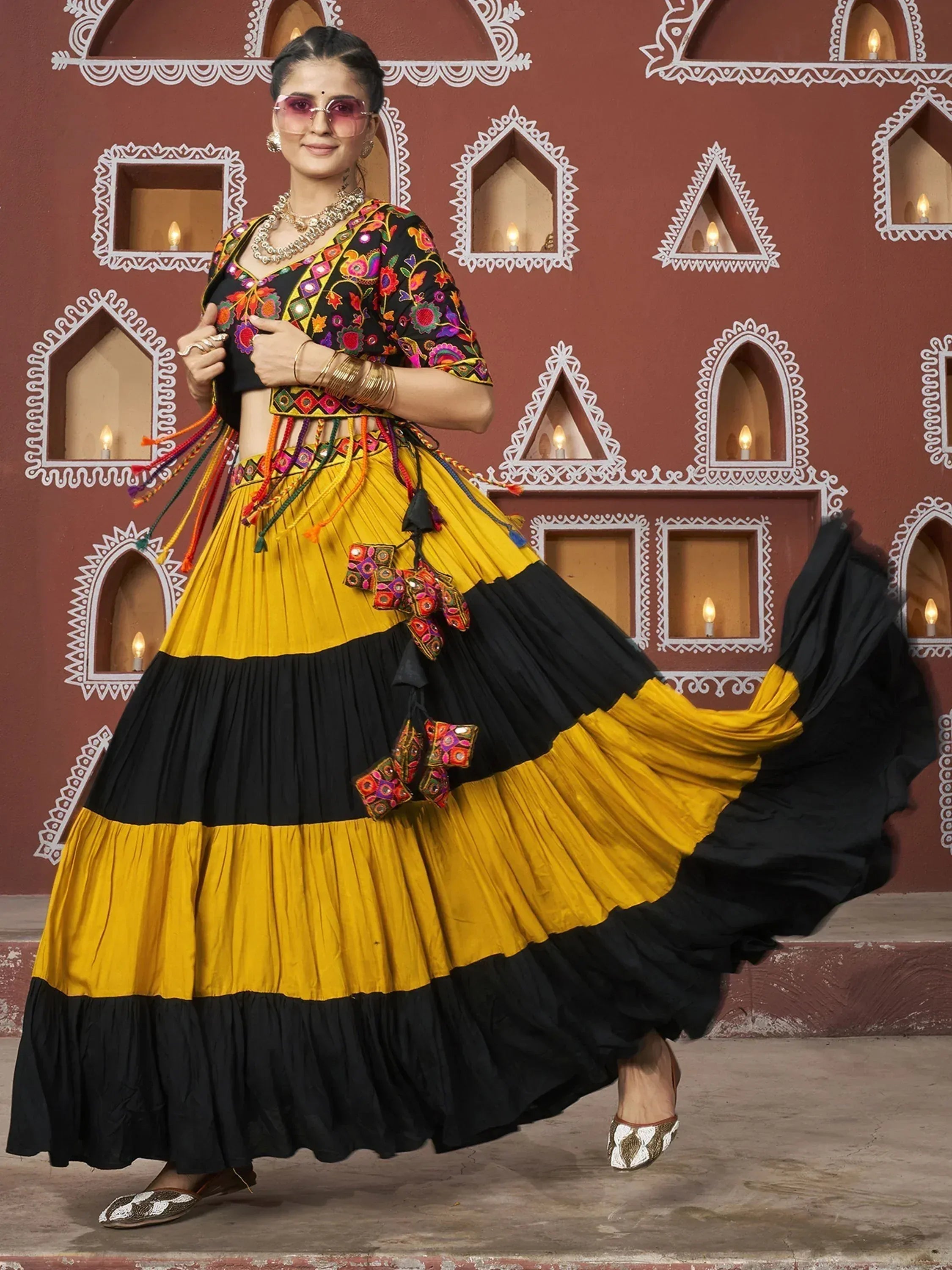 Woman in vibrant yellow and black embroidered lehenga choli with mirror work, styled for festive occasions
