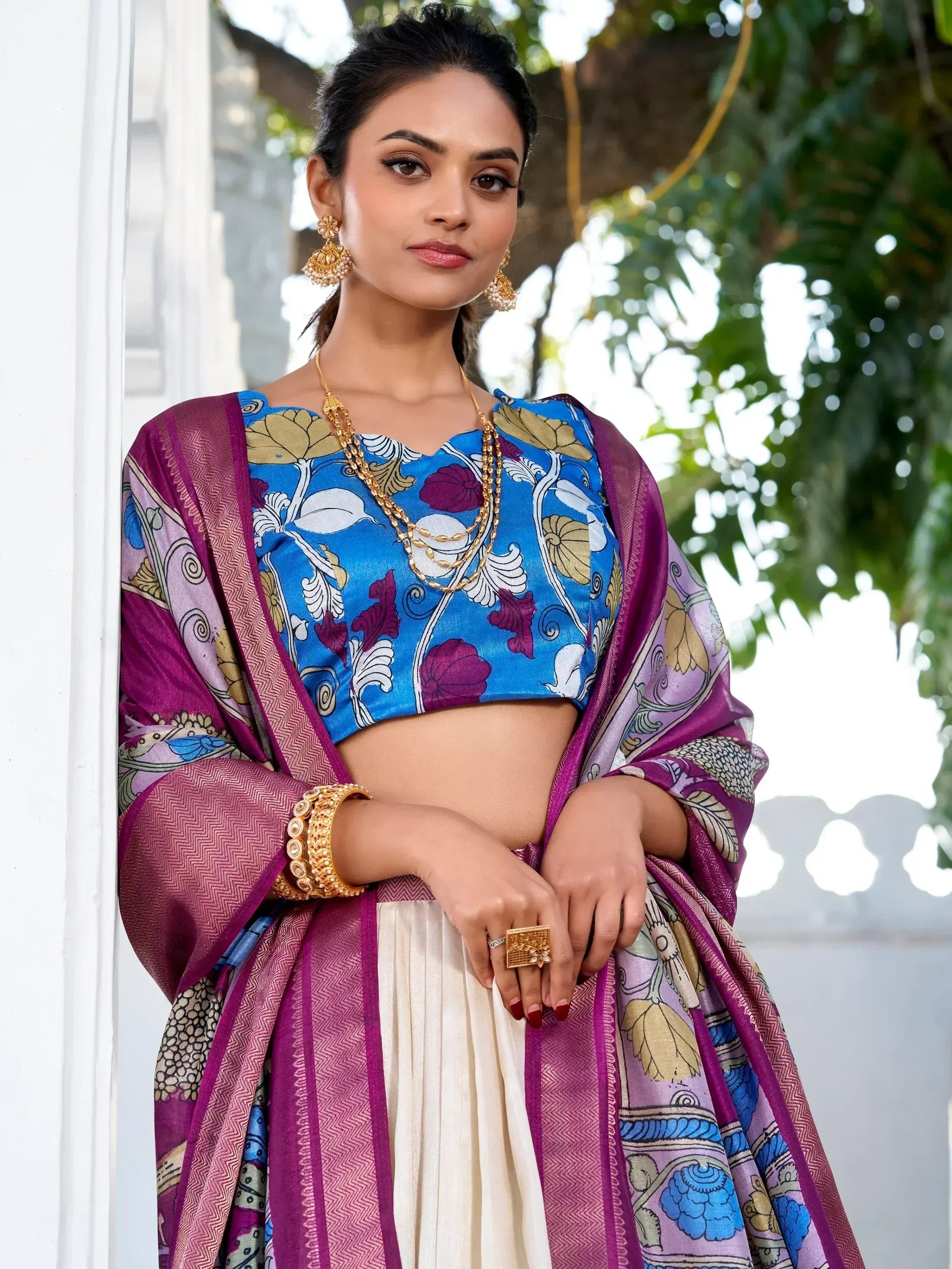 Woman in blue floral crop top with purple patterned dupatta and white skirt, styled with gold jewelry for ethnic wear.