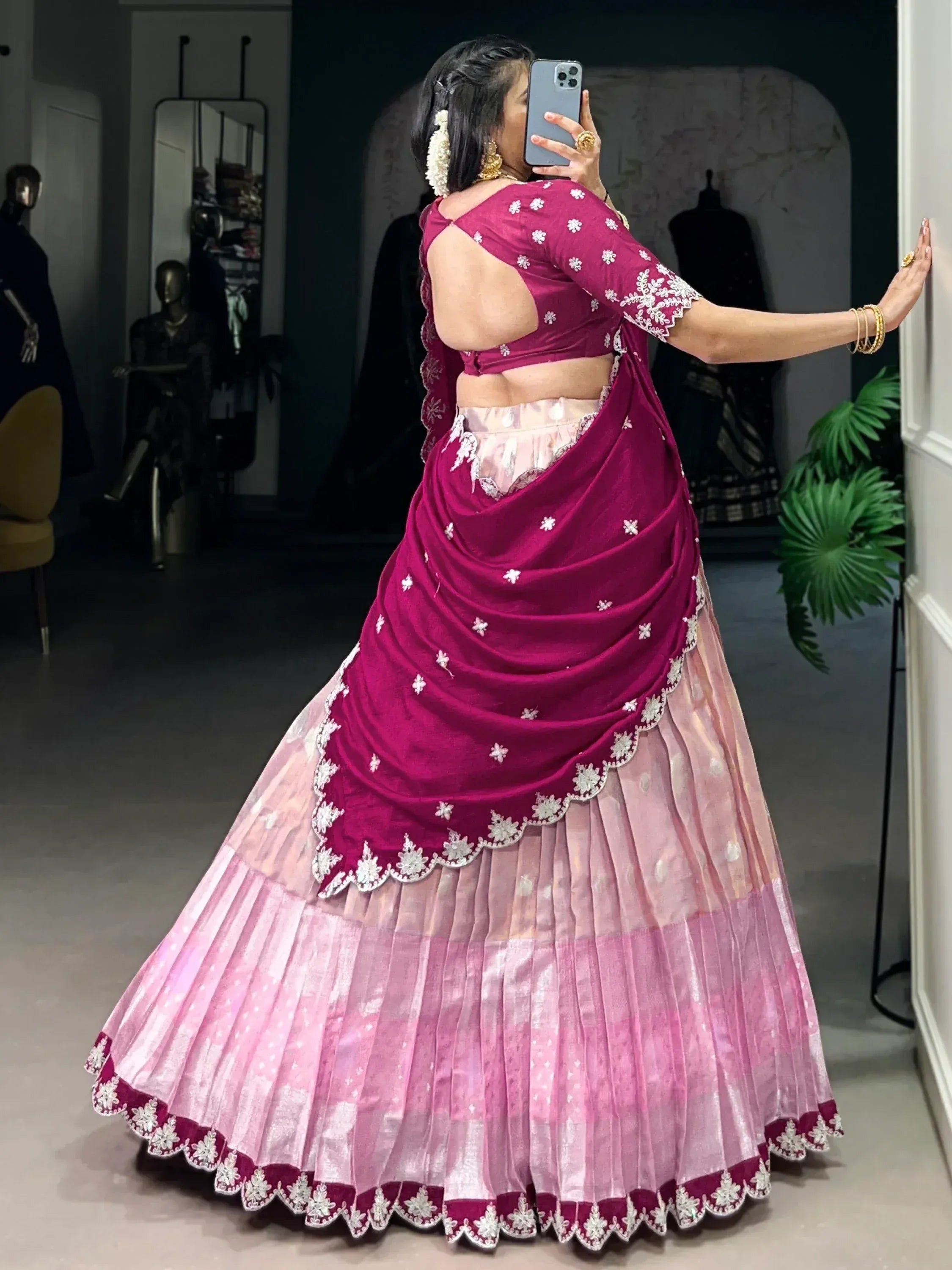Woman in maroon and pink embroidered lehenga choli with floral detailing, taking mirror selfie in boutique