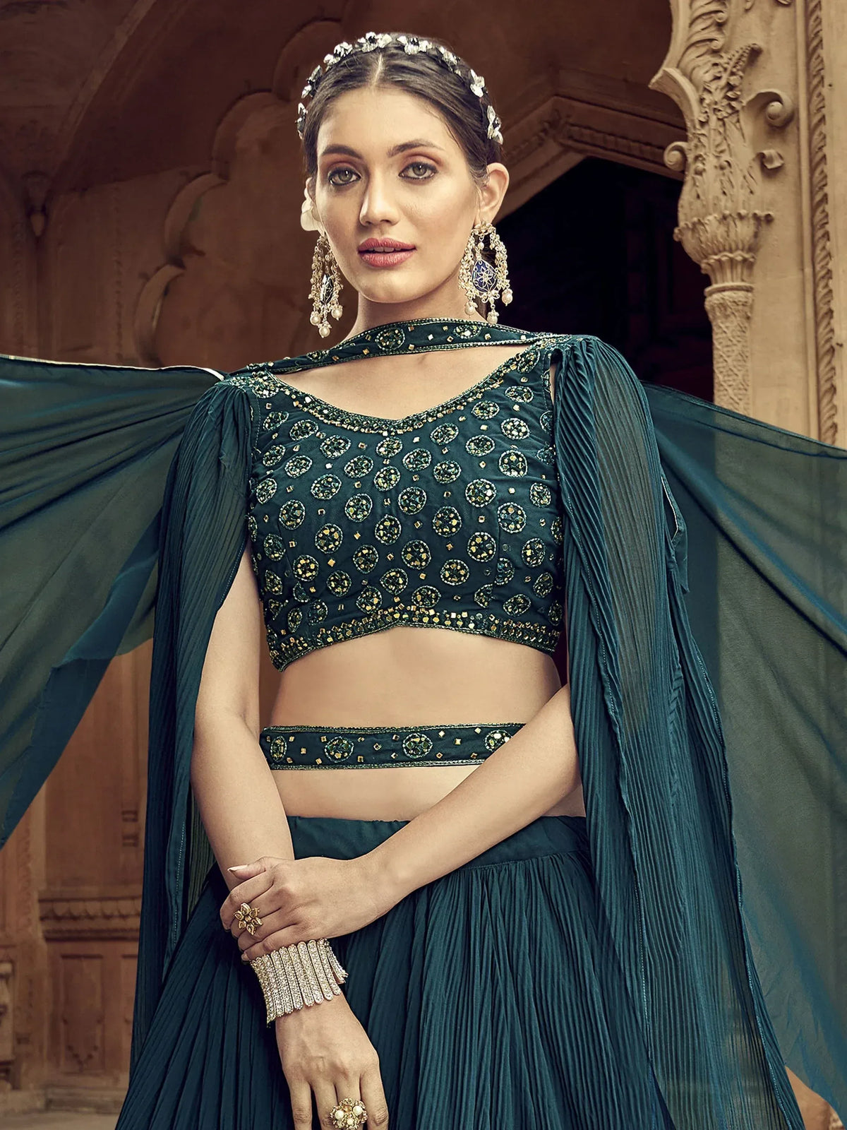 Emerald green designer lehenga choli with heavy embroidery, pleated skirt, and cape, perfect for Indian weddings.