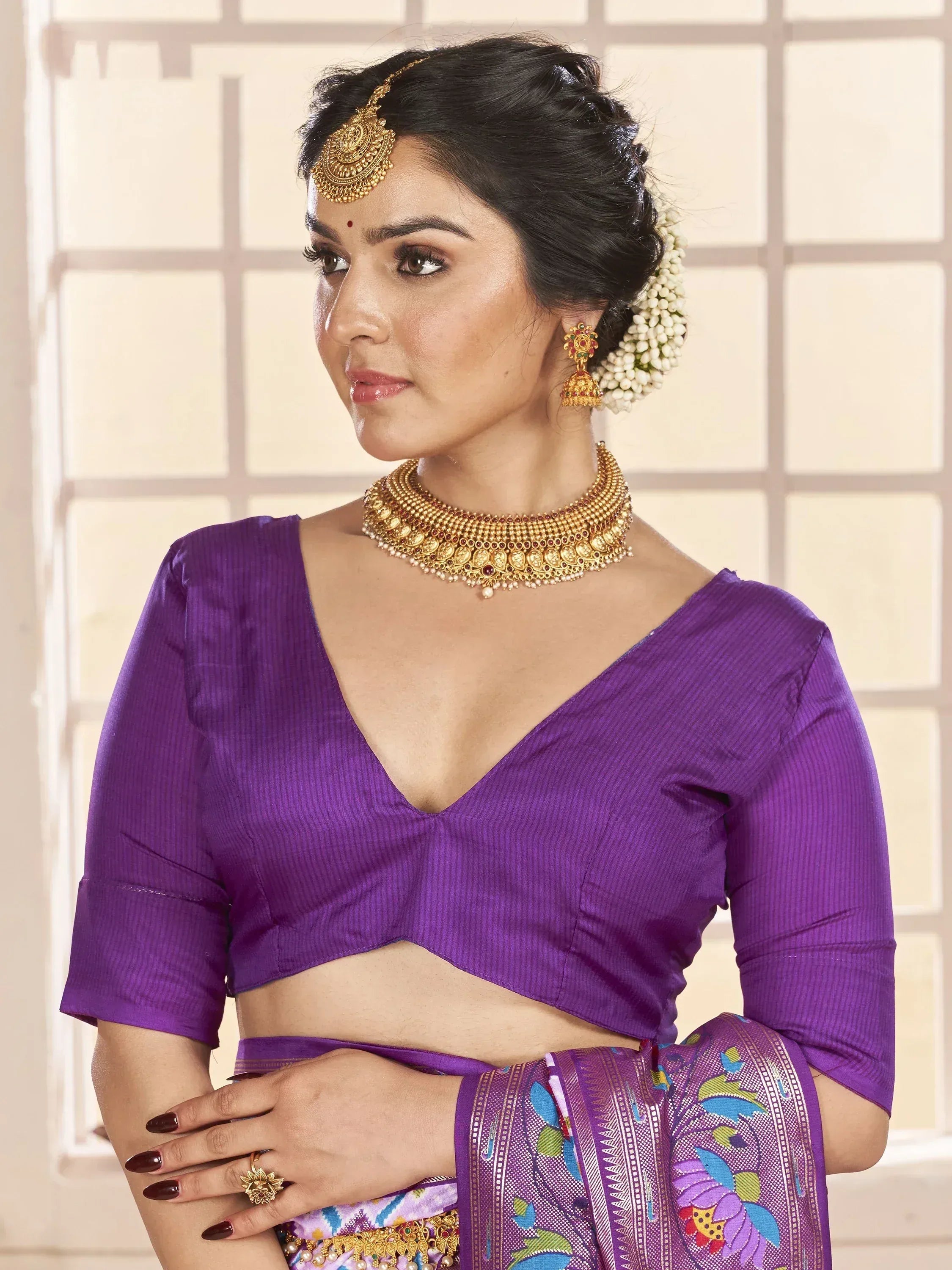 Woman in purple ethnic saree blouse with gold jewelry and floral hair accessories