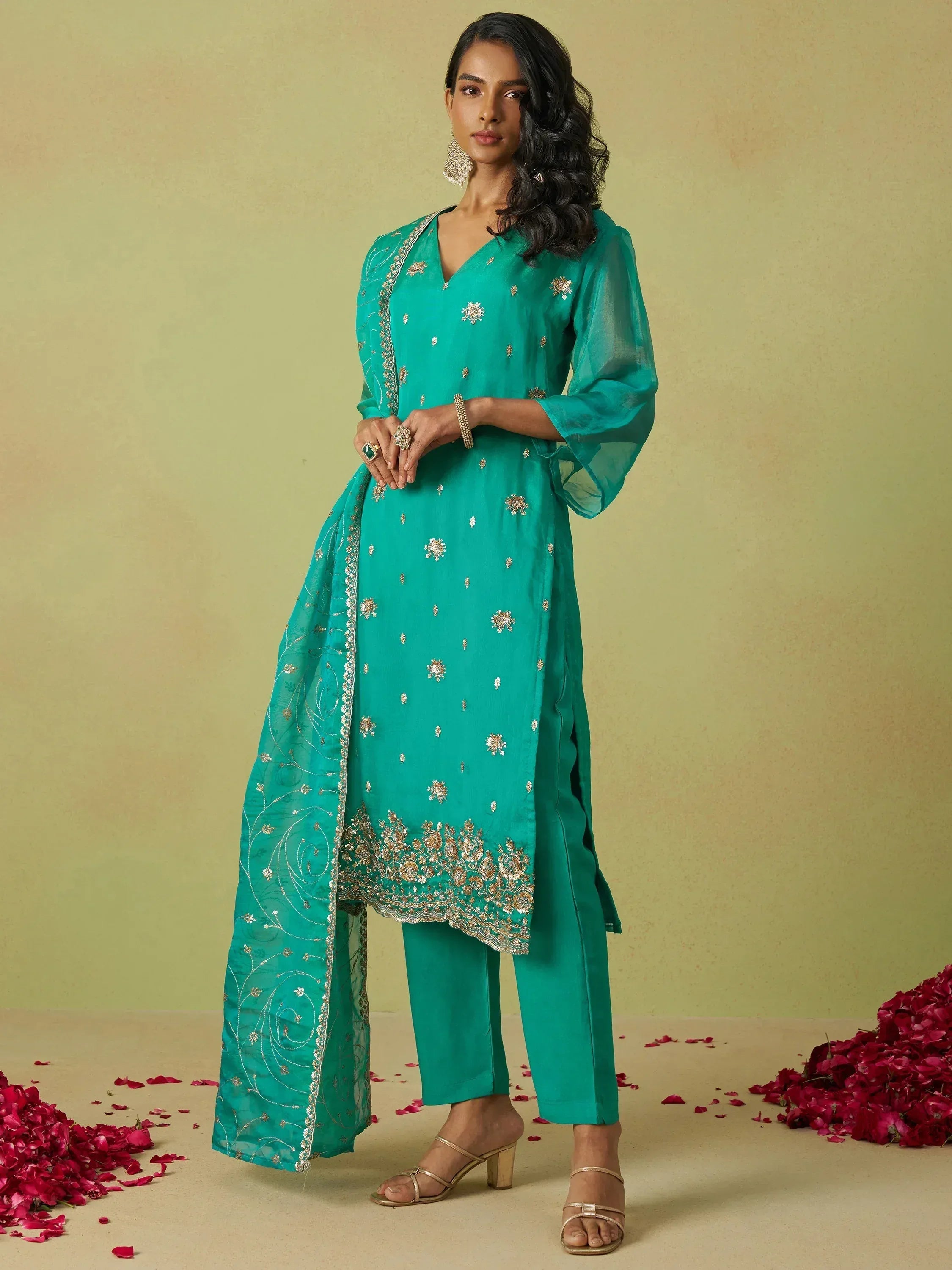 Teal embroidered salwar kameez with gold detailing and matching dupatta, styled with heels and rose petals