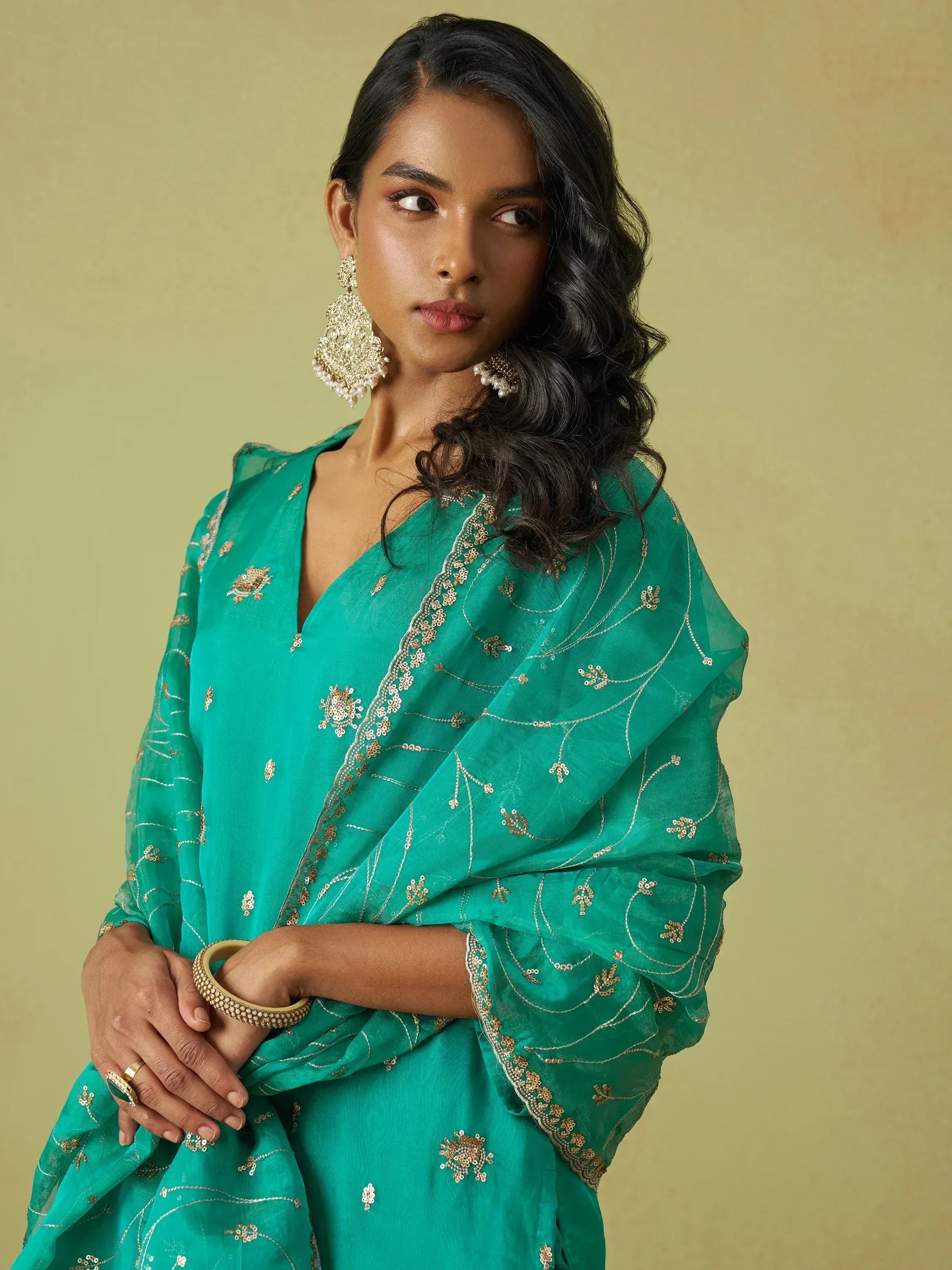 Emerald green embroidered saree with gold detailing, paired with statement earrings for Indian ethnic wear.