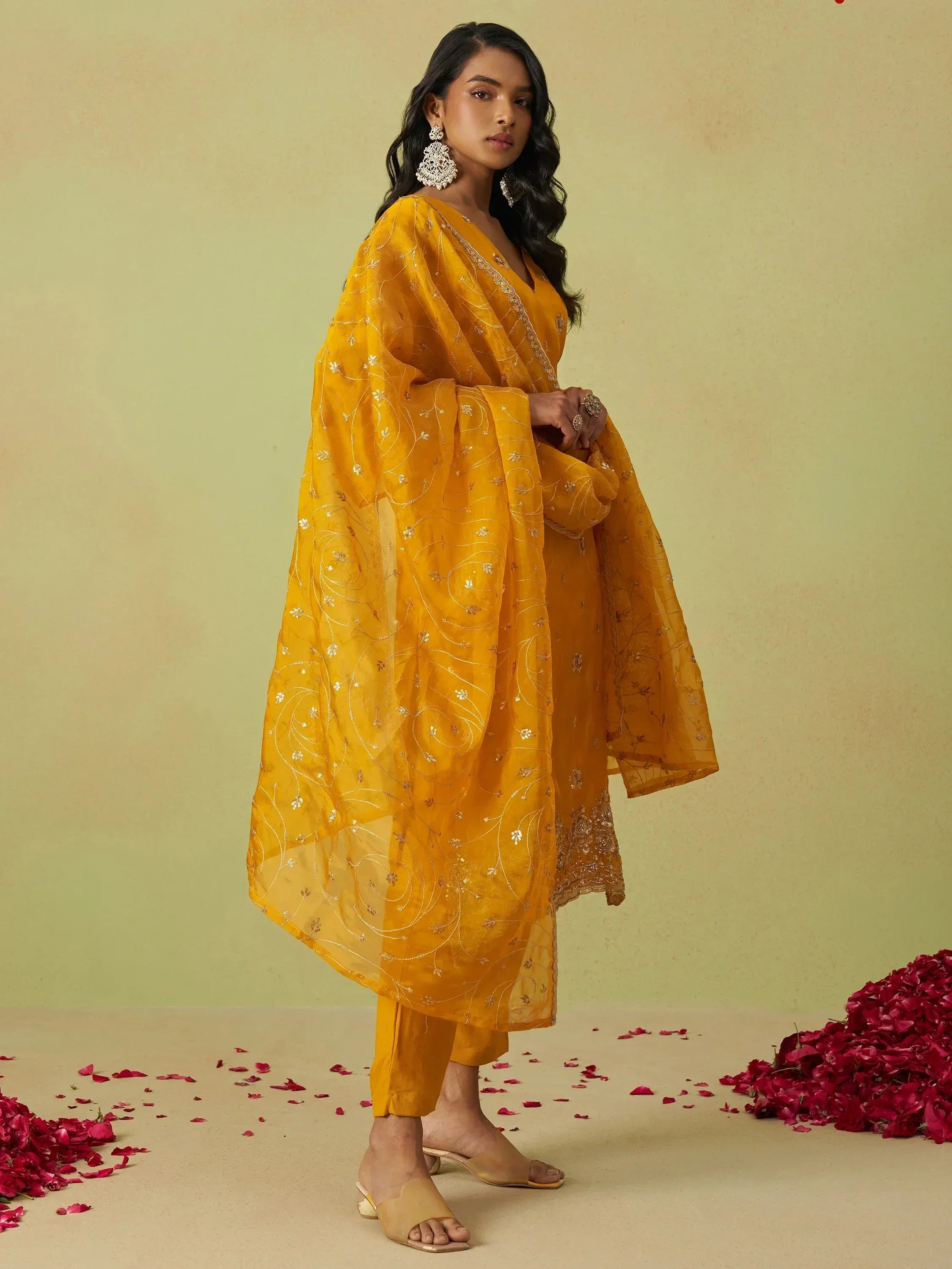 Yellow embroidered salwar kameez with sheer dupatta, floral detailing, and rose petals on floor