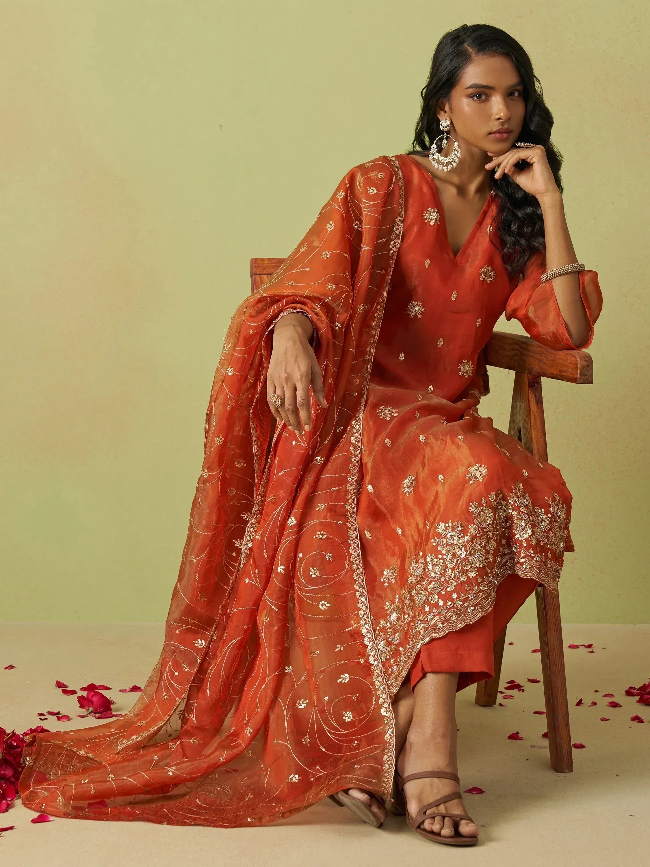 Woman in orange embroidered ethnic salwar kameez with dupatta, floral detailing, rose petals on floor