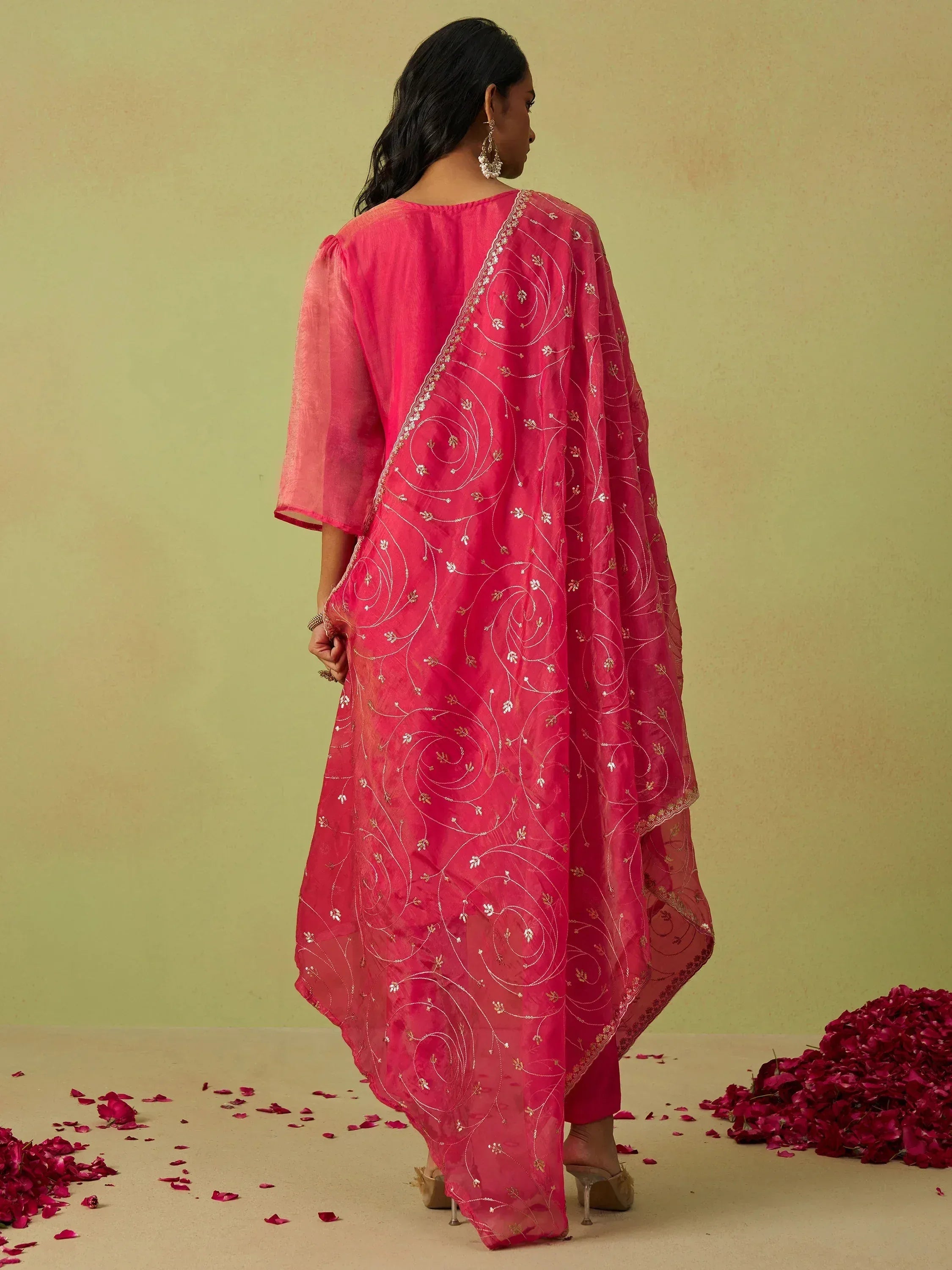 Pink embroidered ethnic gown with sheer dupatta, floral motifs, and rose petals on floor
