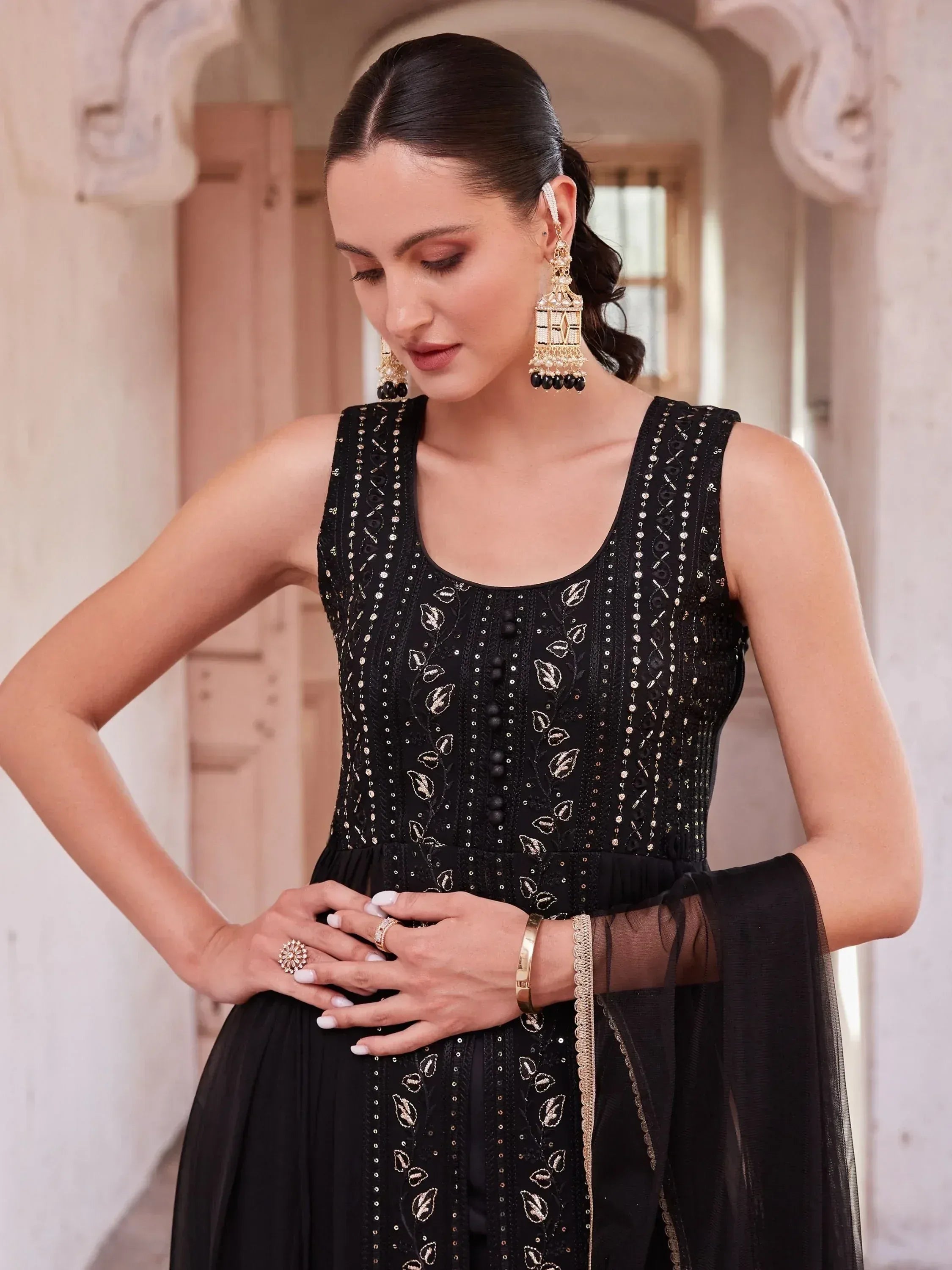 Woman wearing embroidered black ethnic gown with gold details and statement earrings
