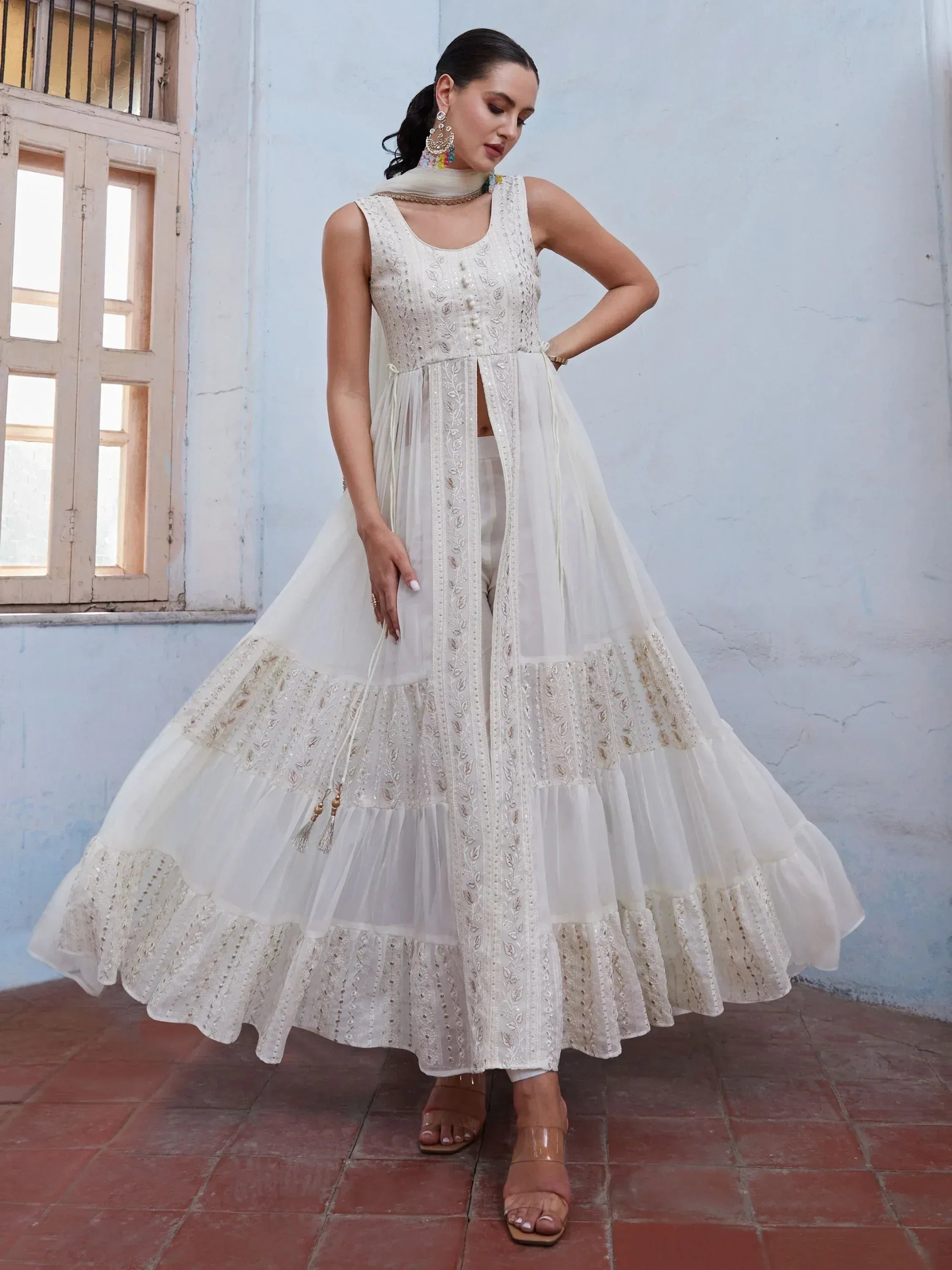 Woman wearing white embroidered ethnic gown with flared hem, dupatta, and chandelier earrings
