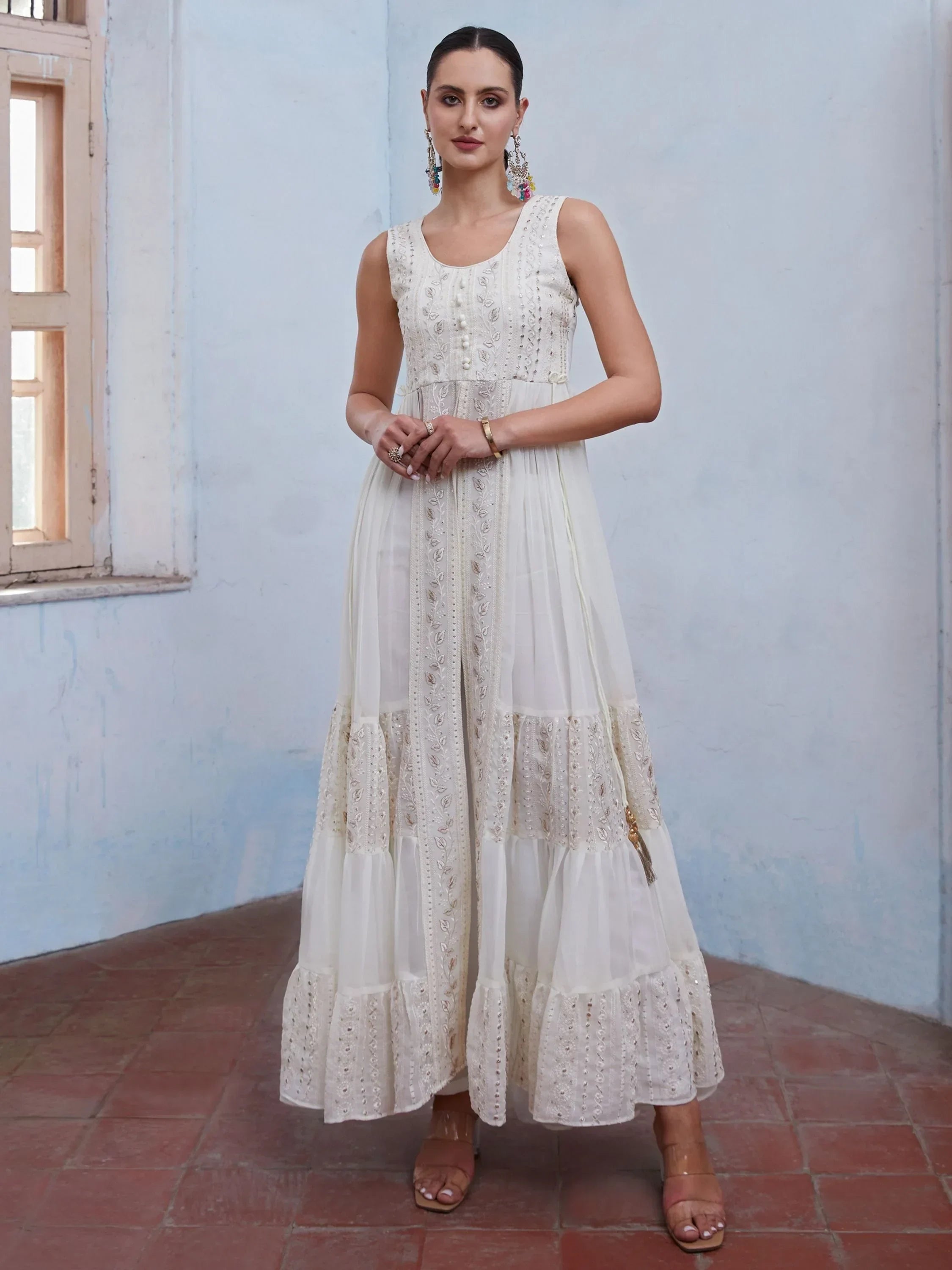 Woman wearing an elegant white ethnic gown with embroidery, standing indoors