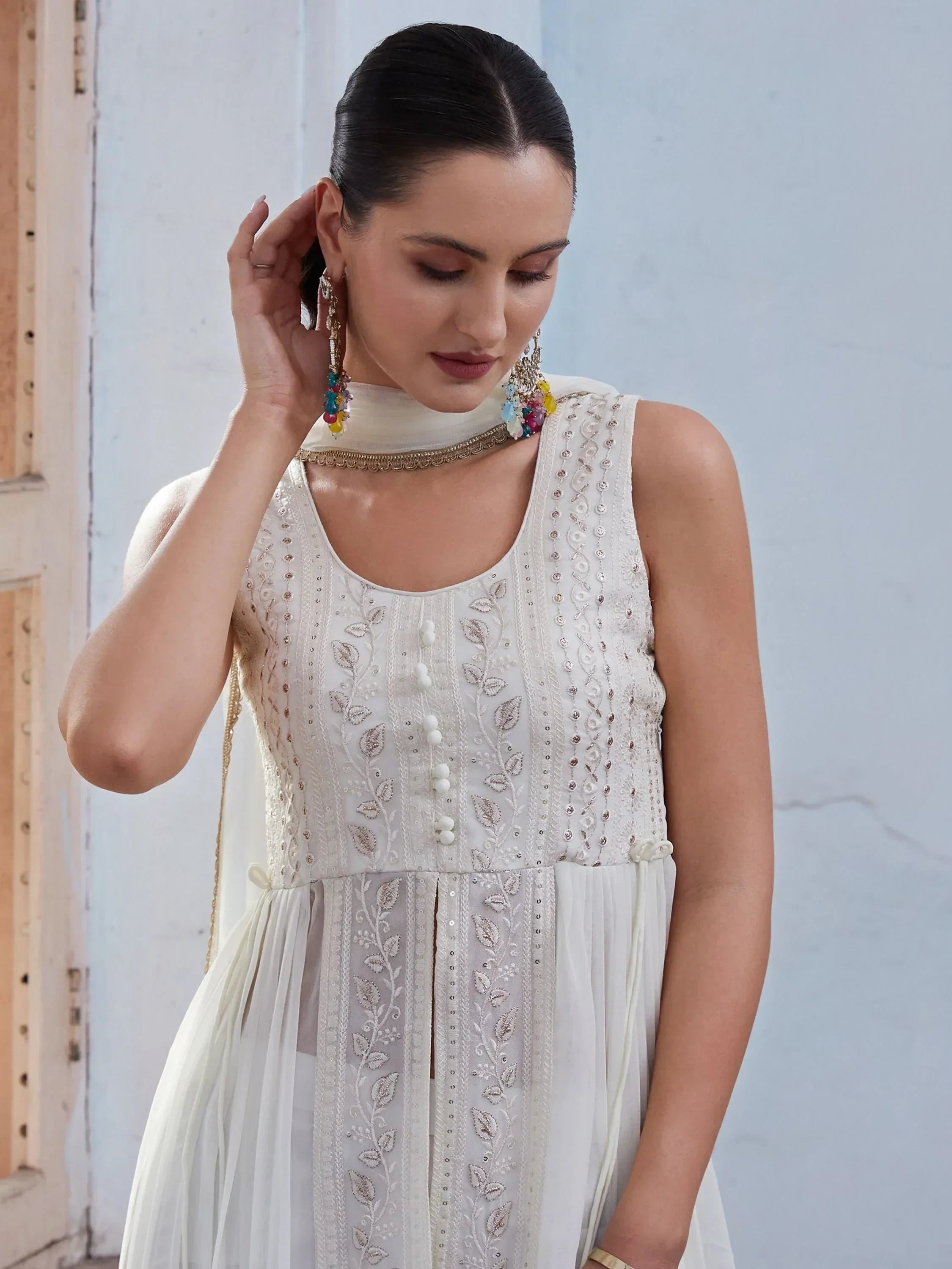 Woman in sleeveless off-white embroidered ethnic gown with dupatta and colorful earrings