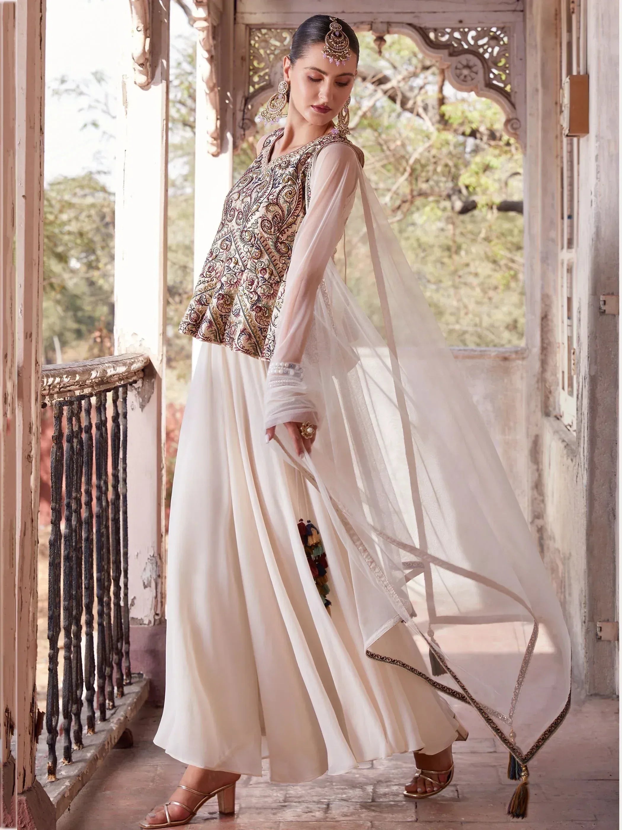 Woman in embroidered ethnic jacket over cream lehenga with dupatta, traditional jewelry