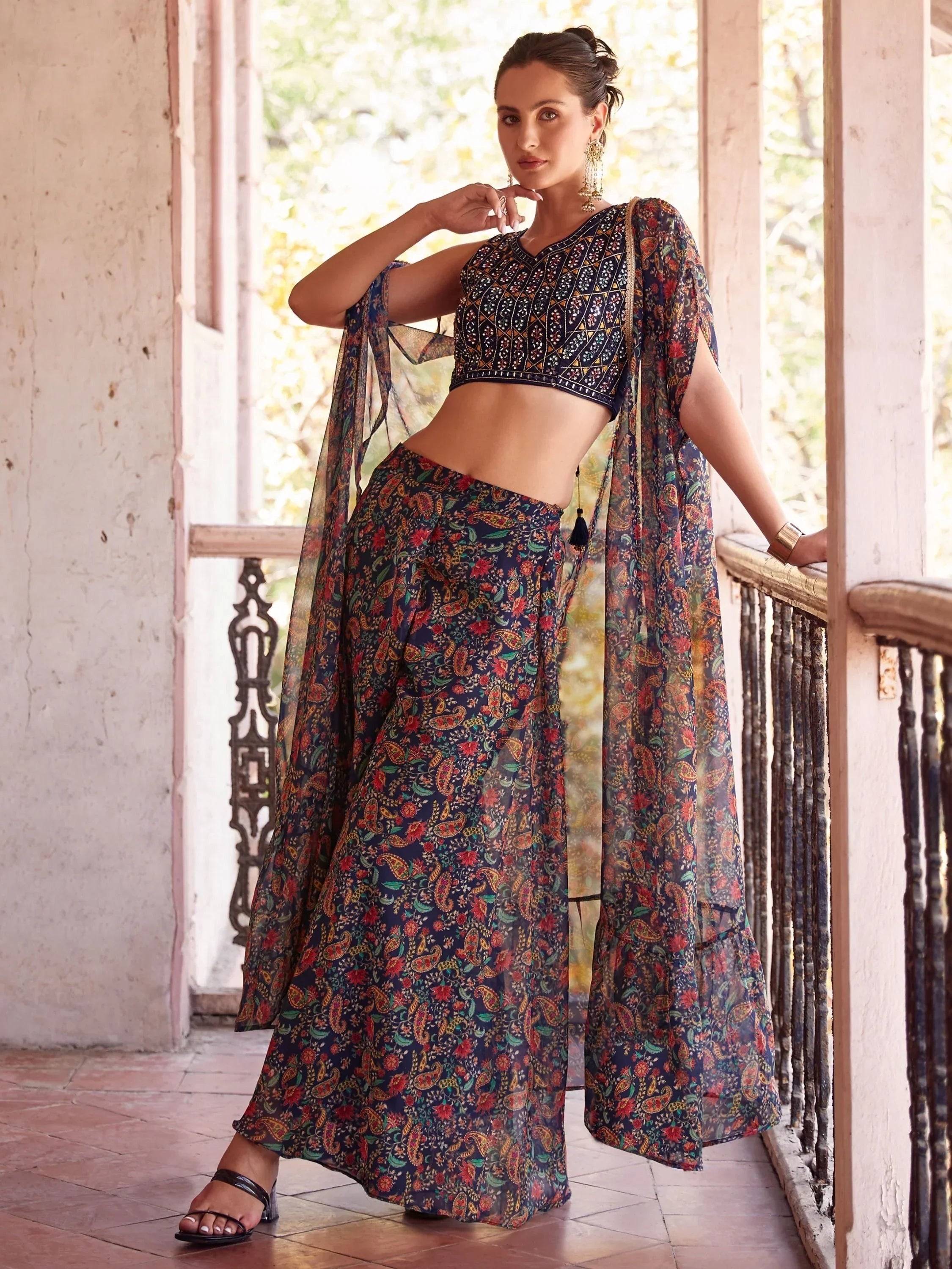 Woman in a designer lehenga choli with printed dupatta, standing in a traditional veranda