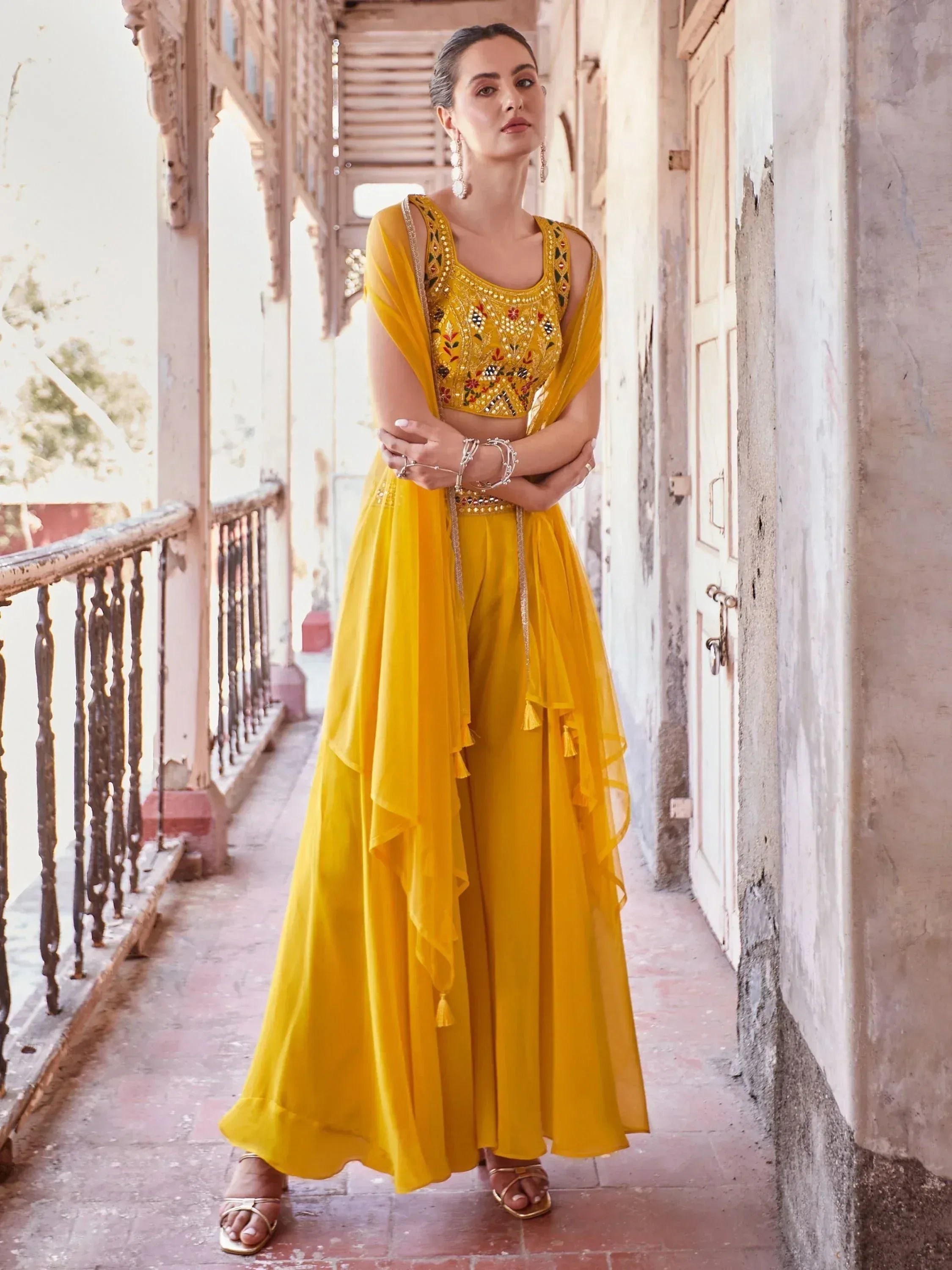 Woman in yellow embroidered ethnic gown with dupatta on rustic balcony