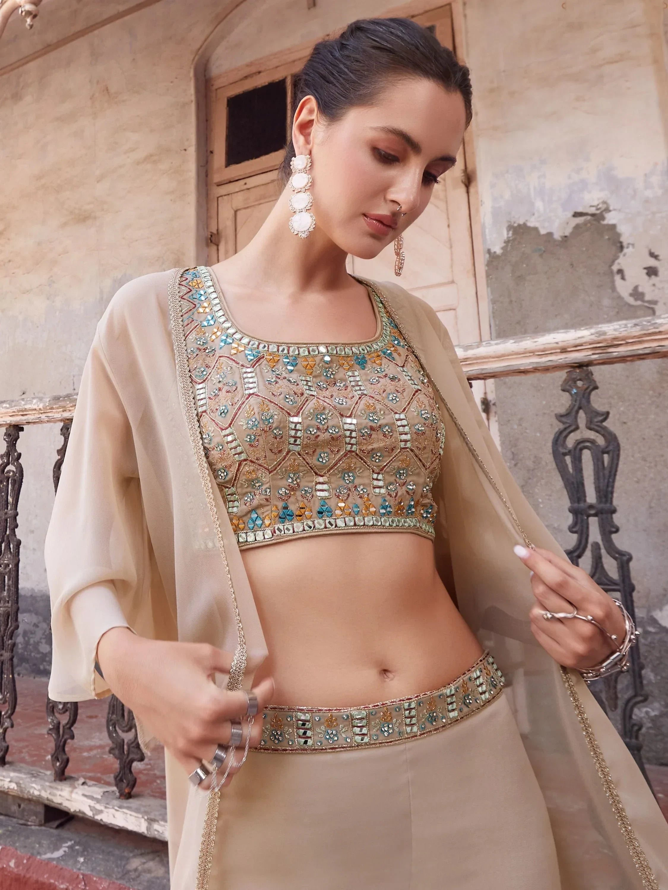 Woman wearing beige designer lehenga choli with mirror and bead embroidery, ethnic jewelry