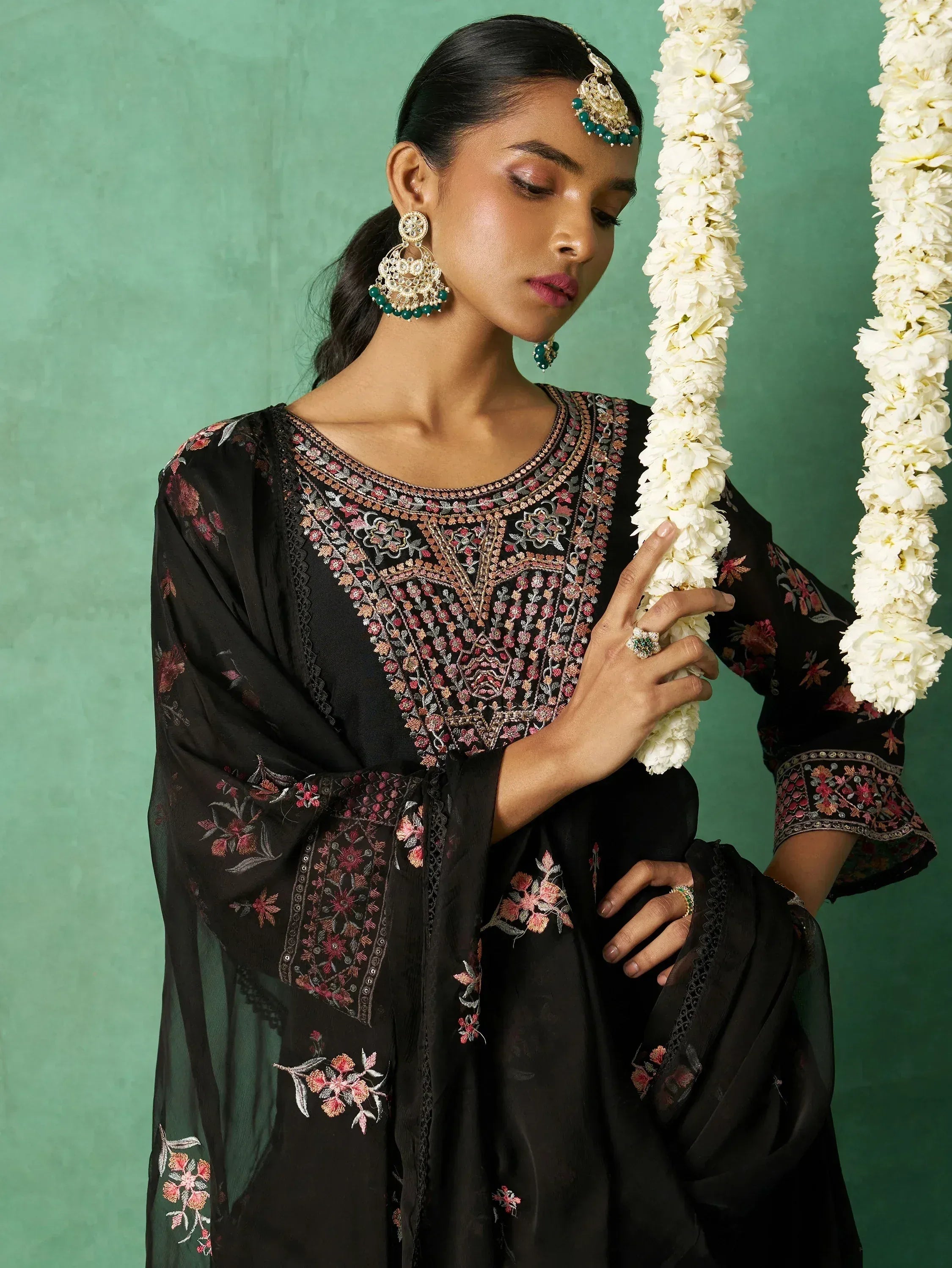 Black embroidered ethnic kurti with floral detailing, paired with traditional jewelry and white flower garlands.