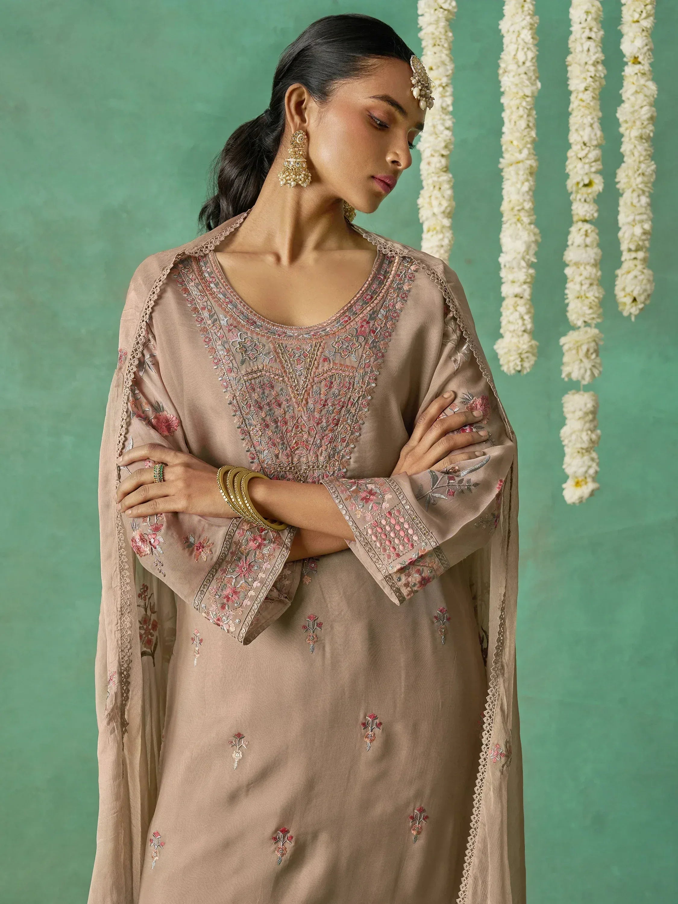 Elegant beige embroidered salwar kameez with floral detailing, paired with traditional jewelry and white flower garlands.