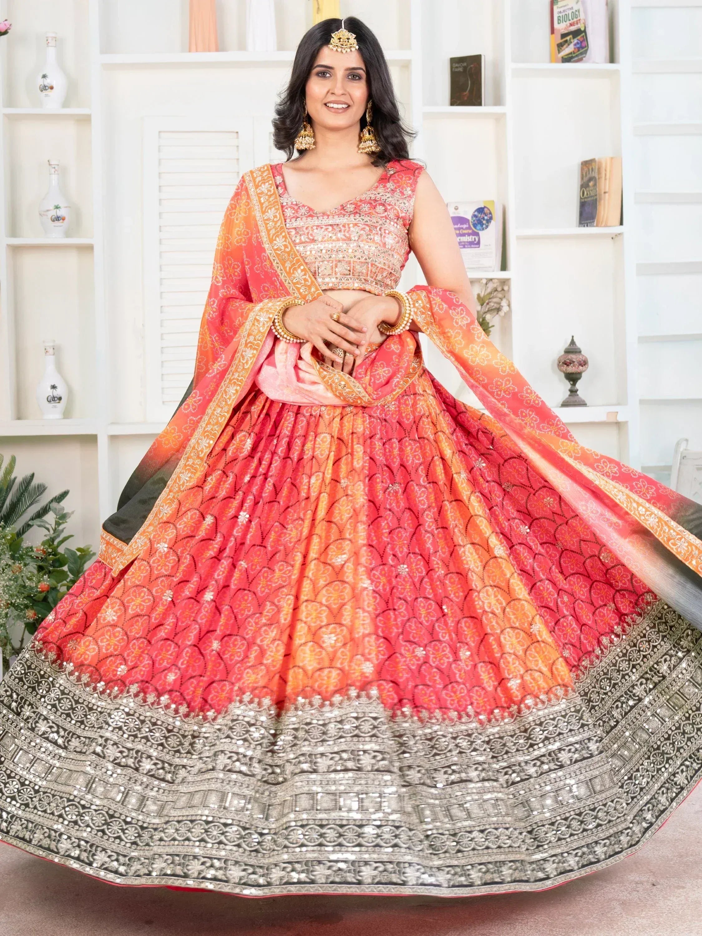 Woman in vibrant orange-pink lehenga choli with floral print and heavy silver border, perfect for Indian ethnic wear occasions.