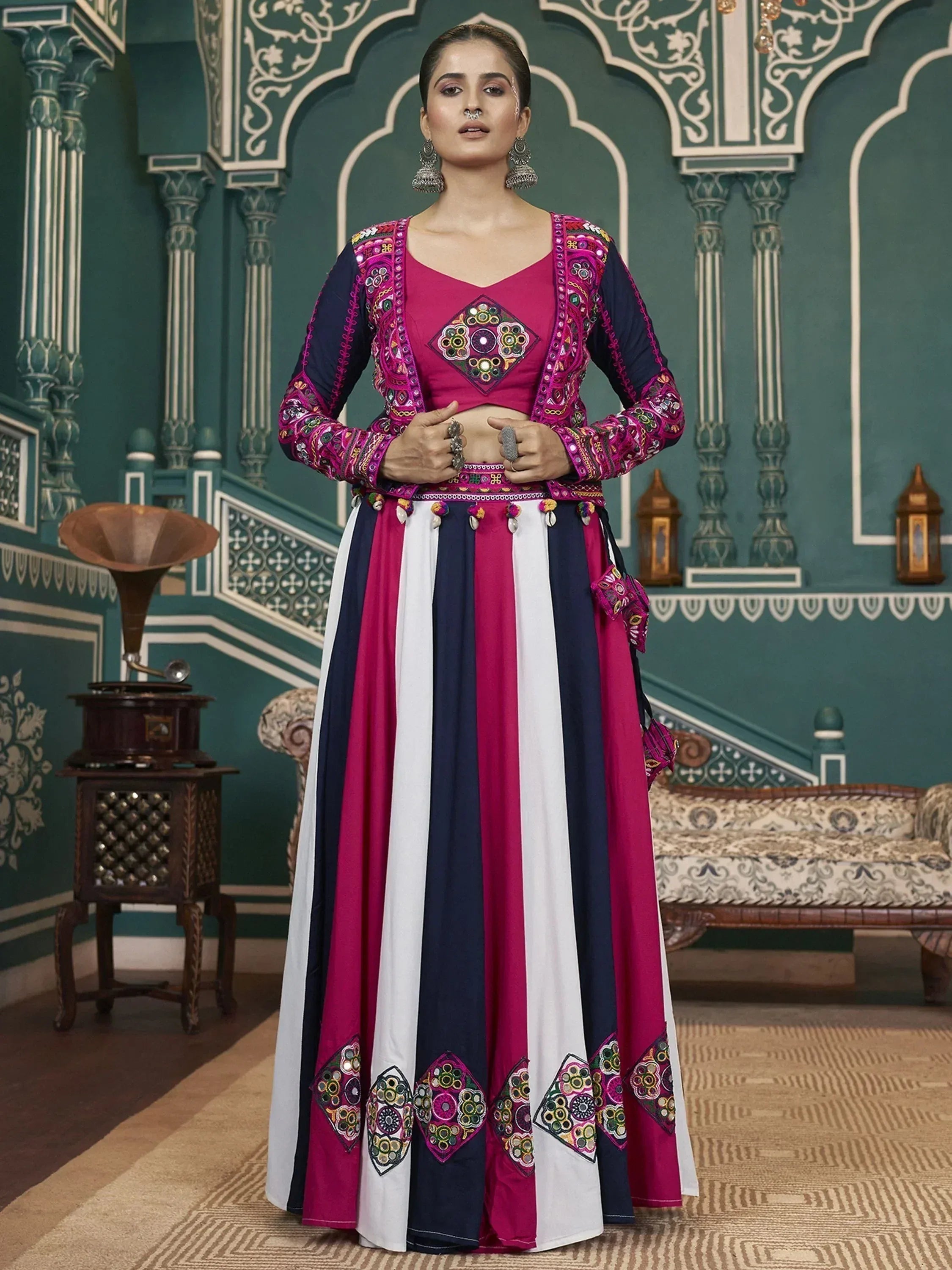 Woman in vibrant pink, navy, and white embroidered ethnic lehenga choli with mirror work, set against ornate Indian palace backdrop