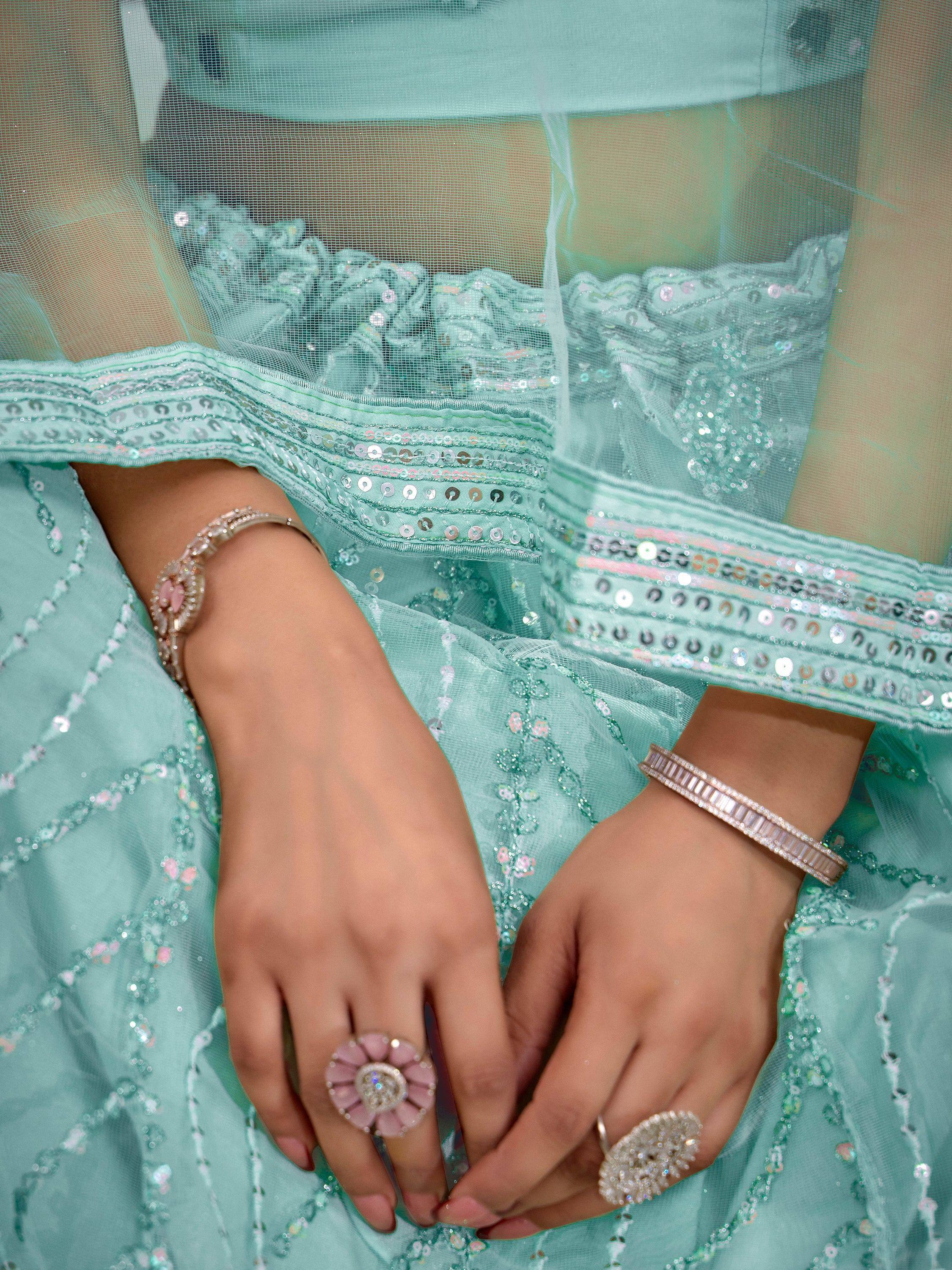 Mint green ethnic gown with sequin embroidery, paired with statement rings and bracelets for festive occasions.