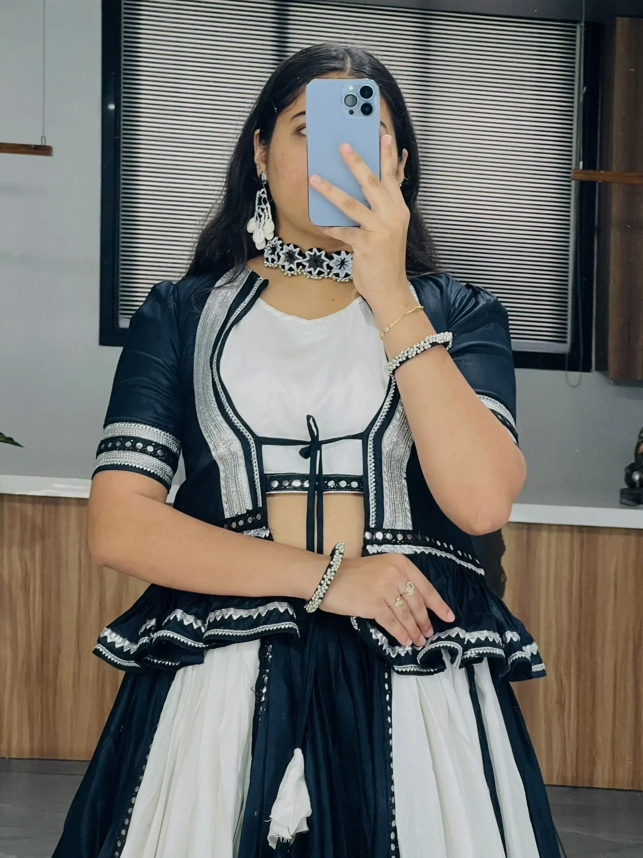 Black and white ethnic lehenga choli with silver embroidery, mirror work, and ruffled hem, styled with statement jewelry.
