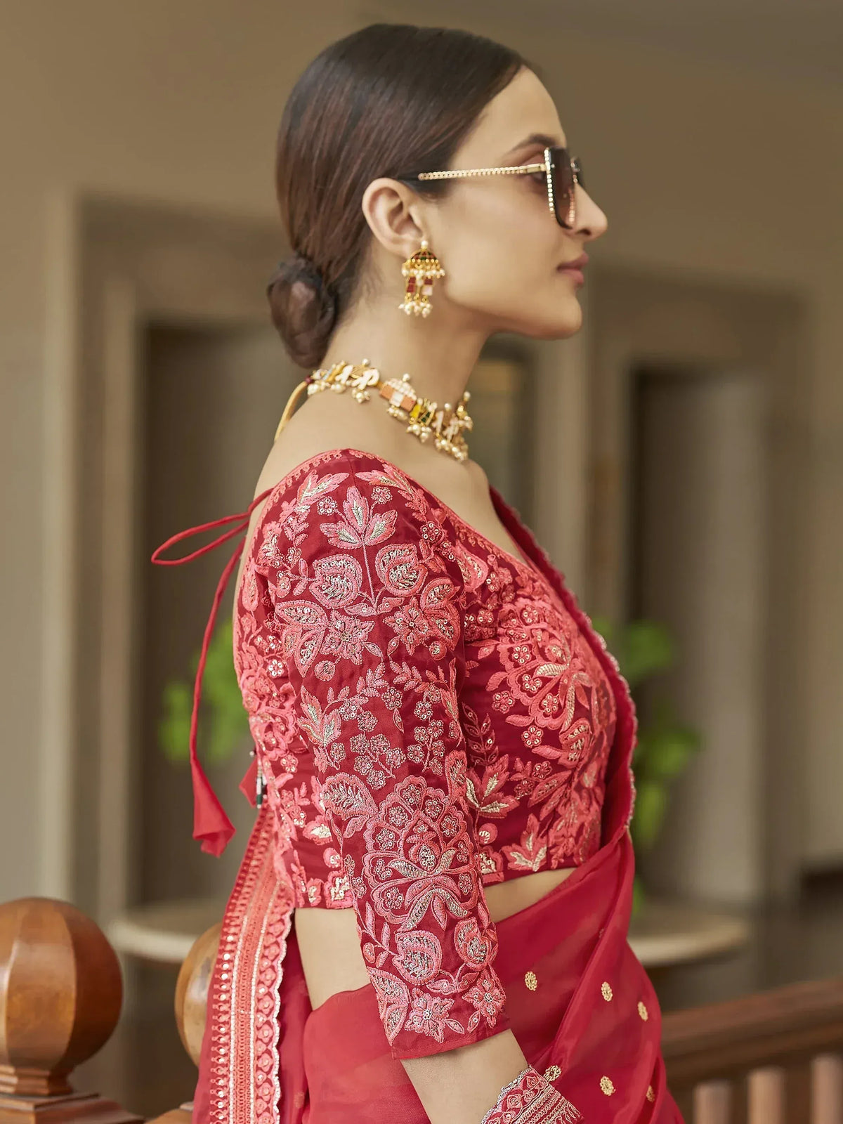 Red embroidered saree blouse with floral design, gold jewelry, and sunglasses for ethnic wear
