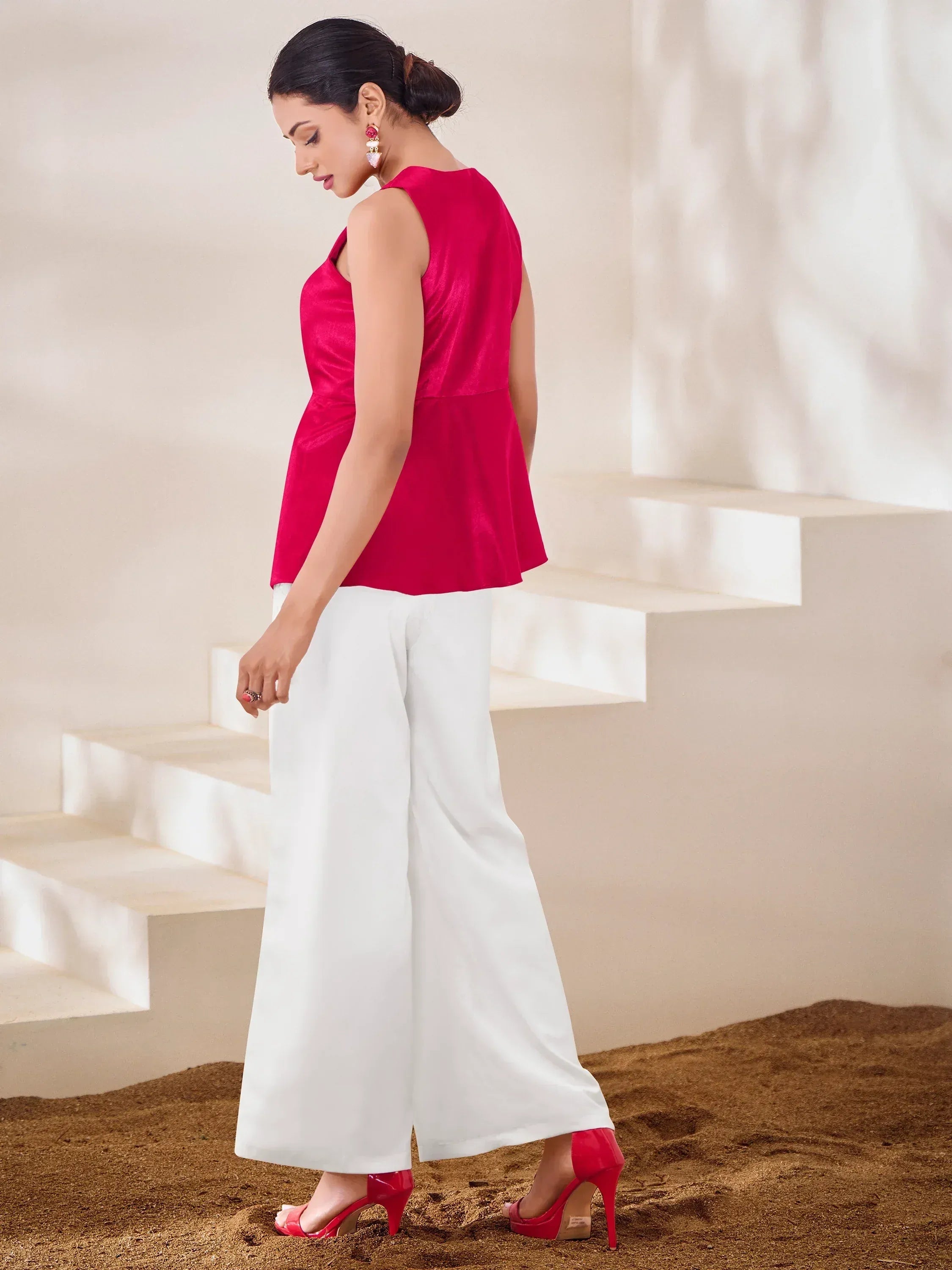 Woman in vibrant red sleeveless top with white palazzo pants and matching heels, styled for ethnic wear