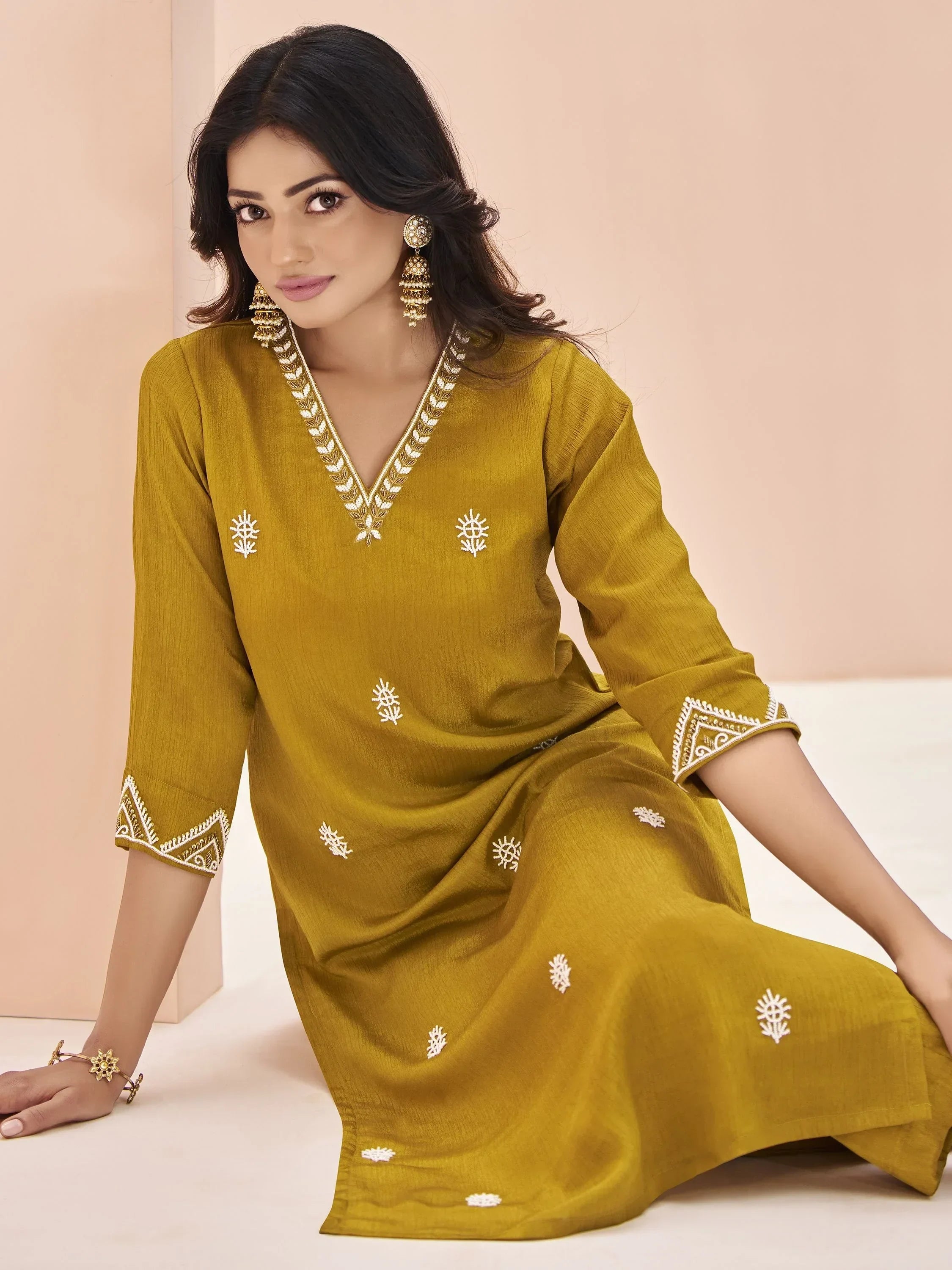 Woman in mustard yellow embroidered kurti with V-neck and ethnic jewelry, seated indoors