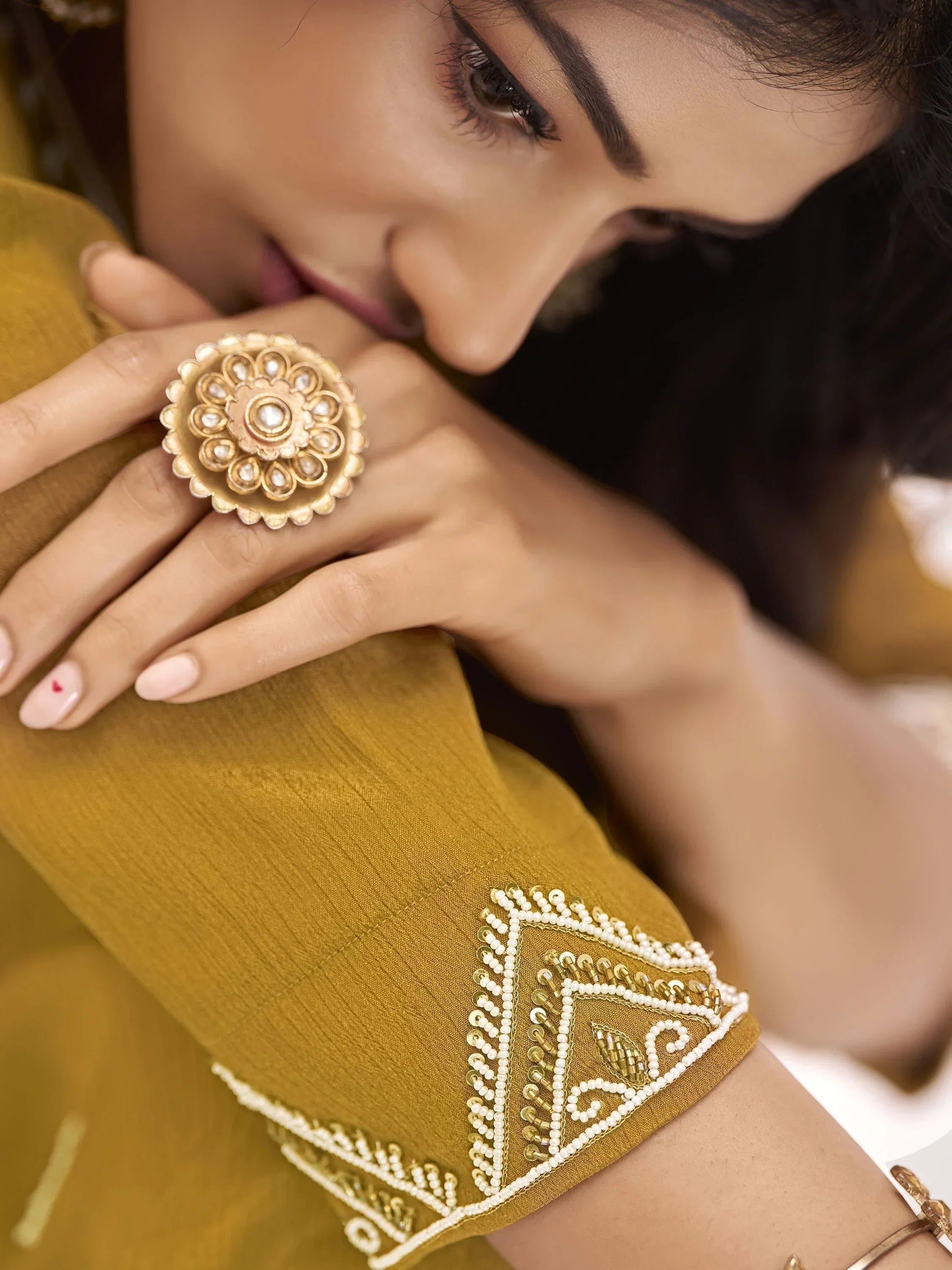 Woman wearing mustard yellow embroidered sleeve and ornate gold statement ring