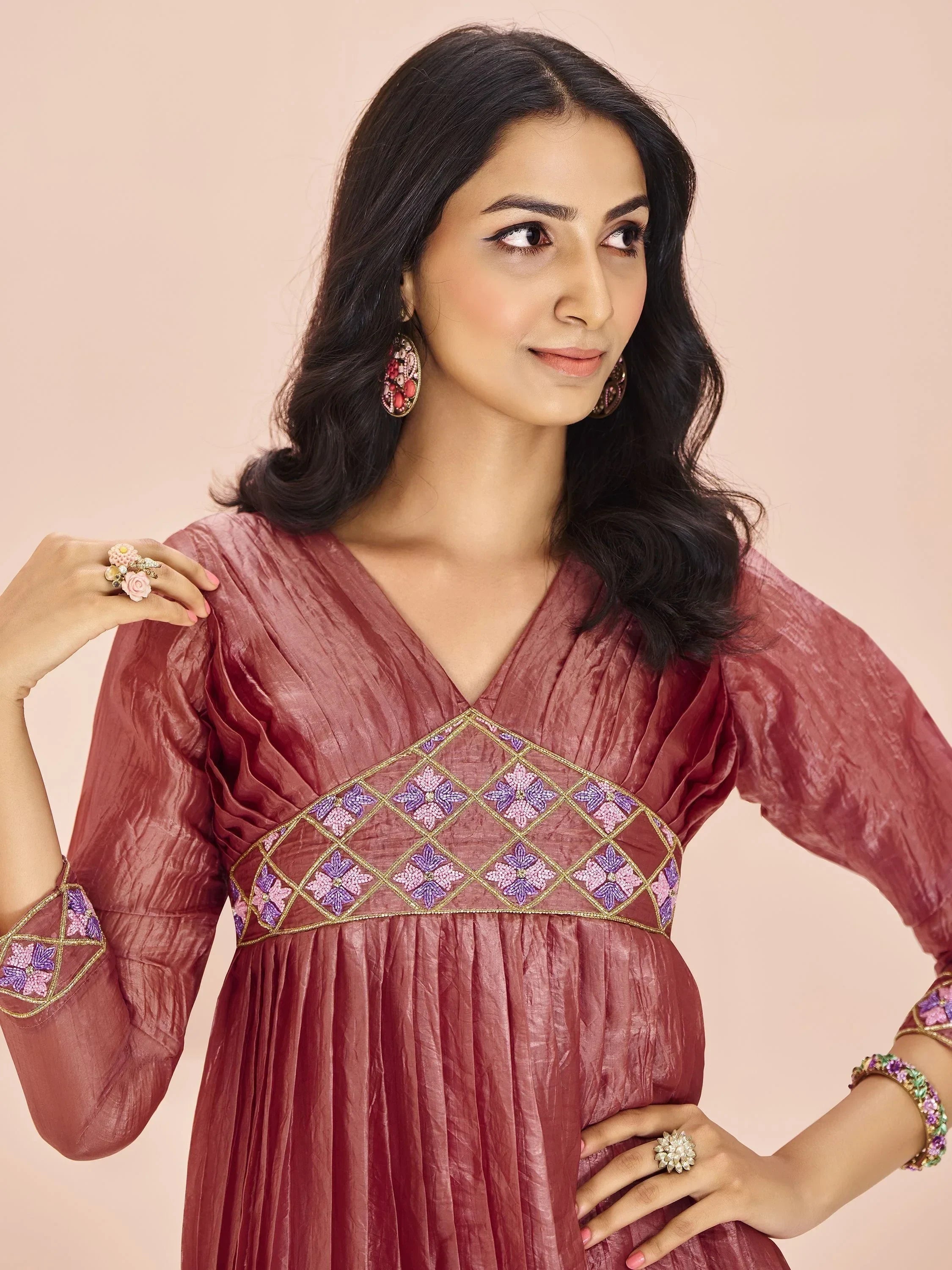 Woman in maroon ethnic gown with purple embroidered details, statement earrings and ring