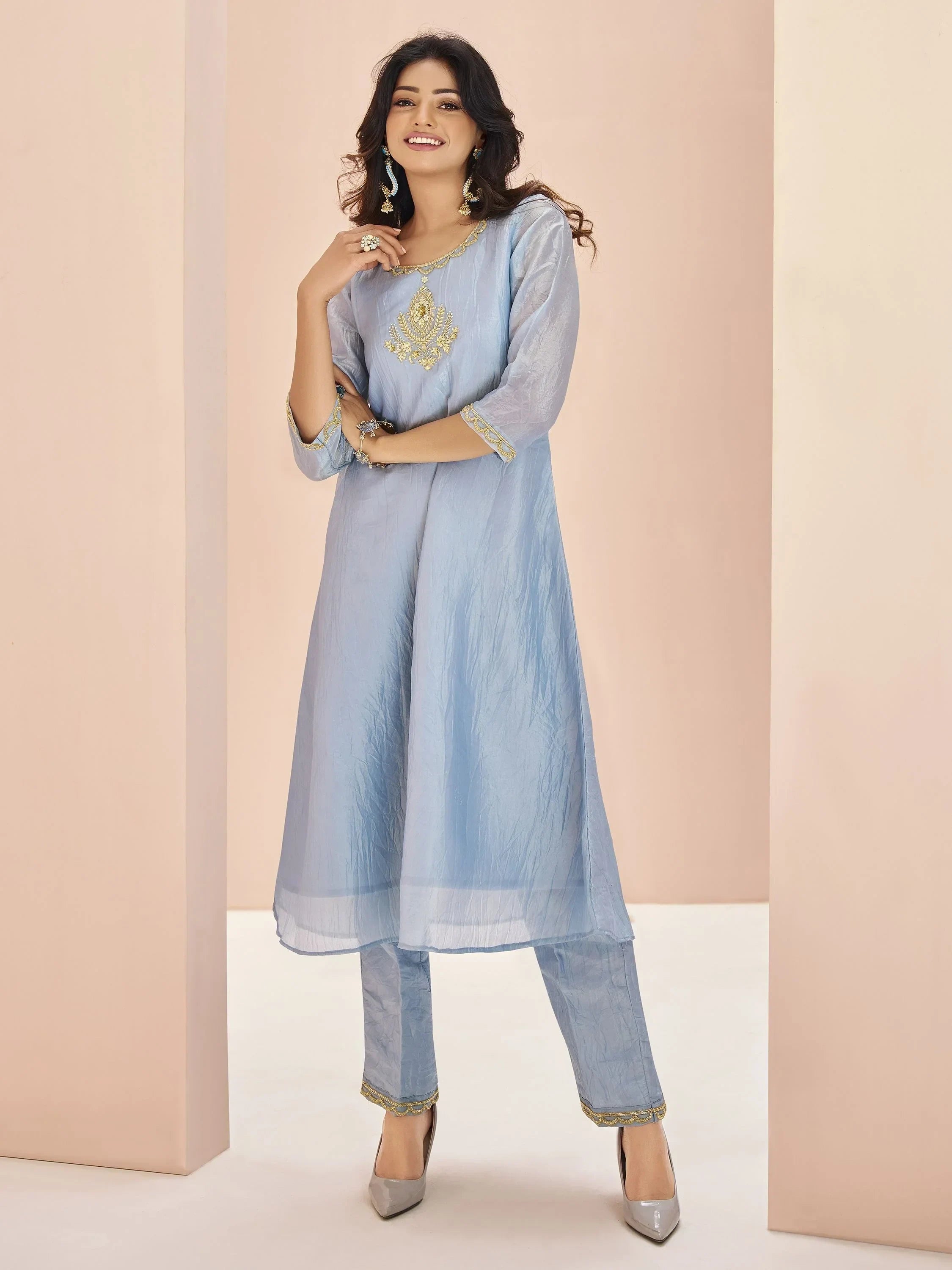 Woman wearing light blue embroidered kurta with matching pants, silver heels, and ethnic jewelry