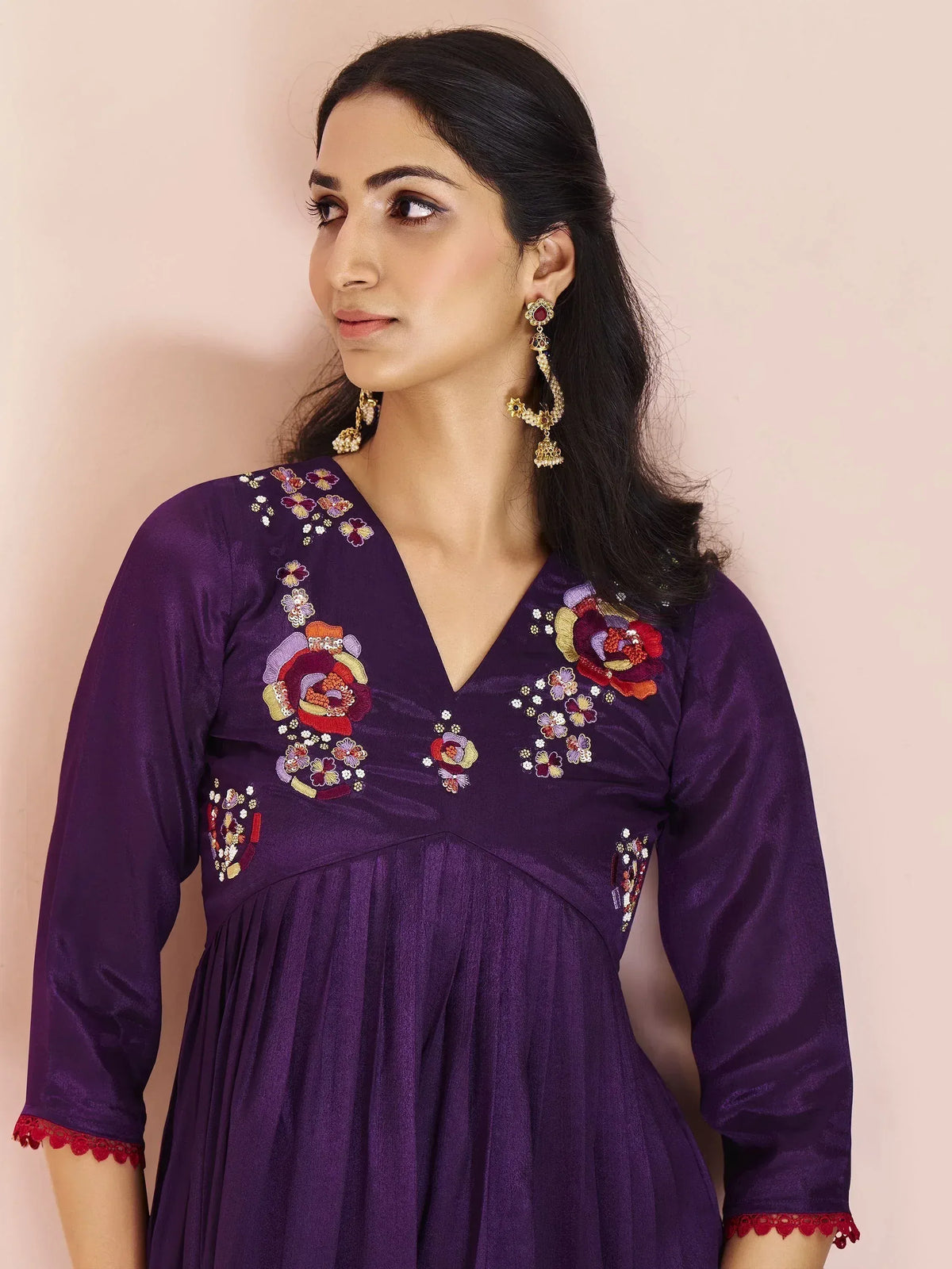 Purple ethnic gown with floral embroidery and red lace cuffs, paired with gold jhumka earrings