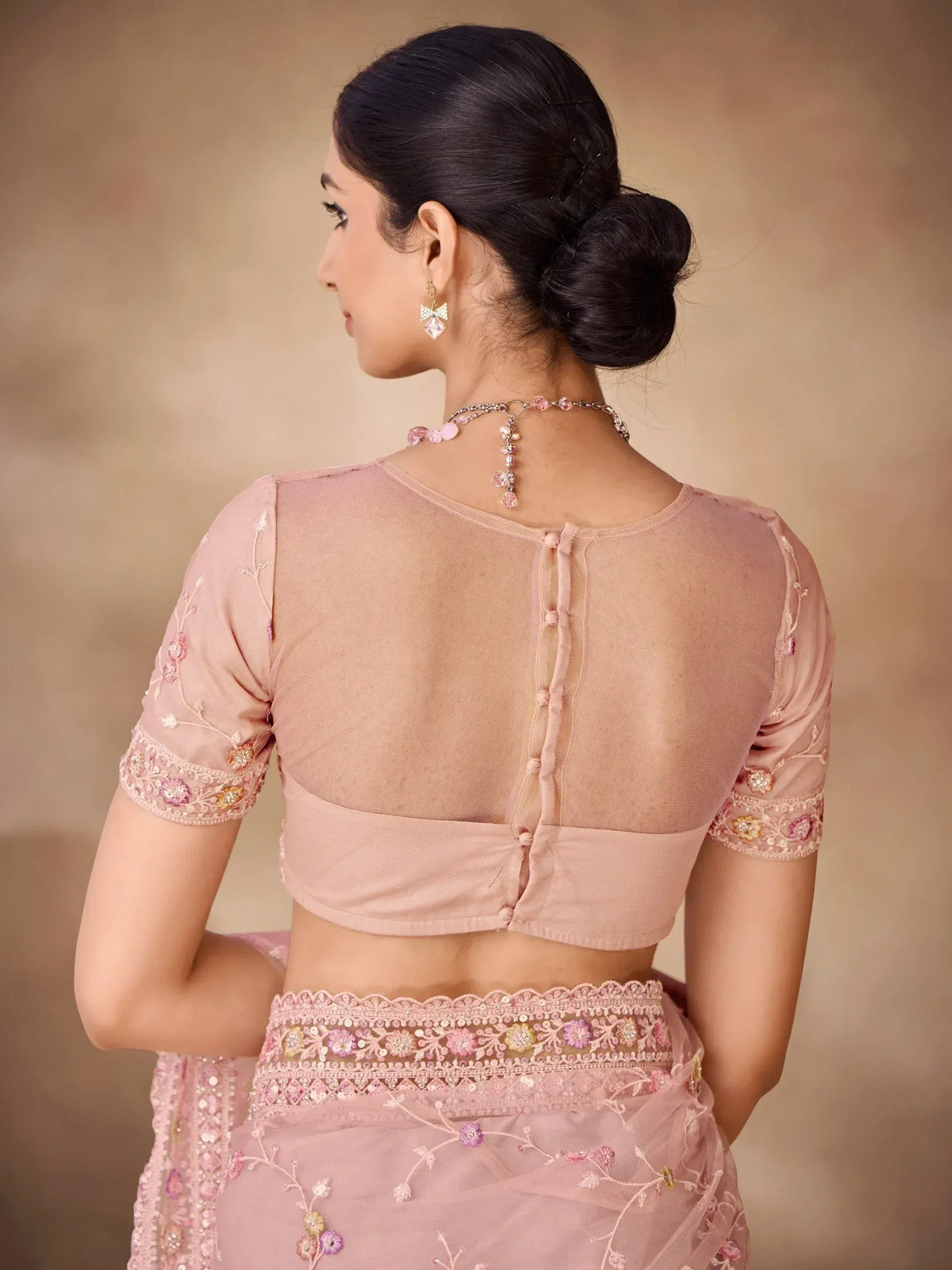Pink embroidered saree with sheer back blouse, floral detailing, and matching jewelry for ethnic wear