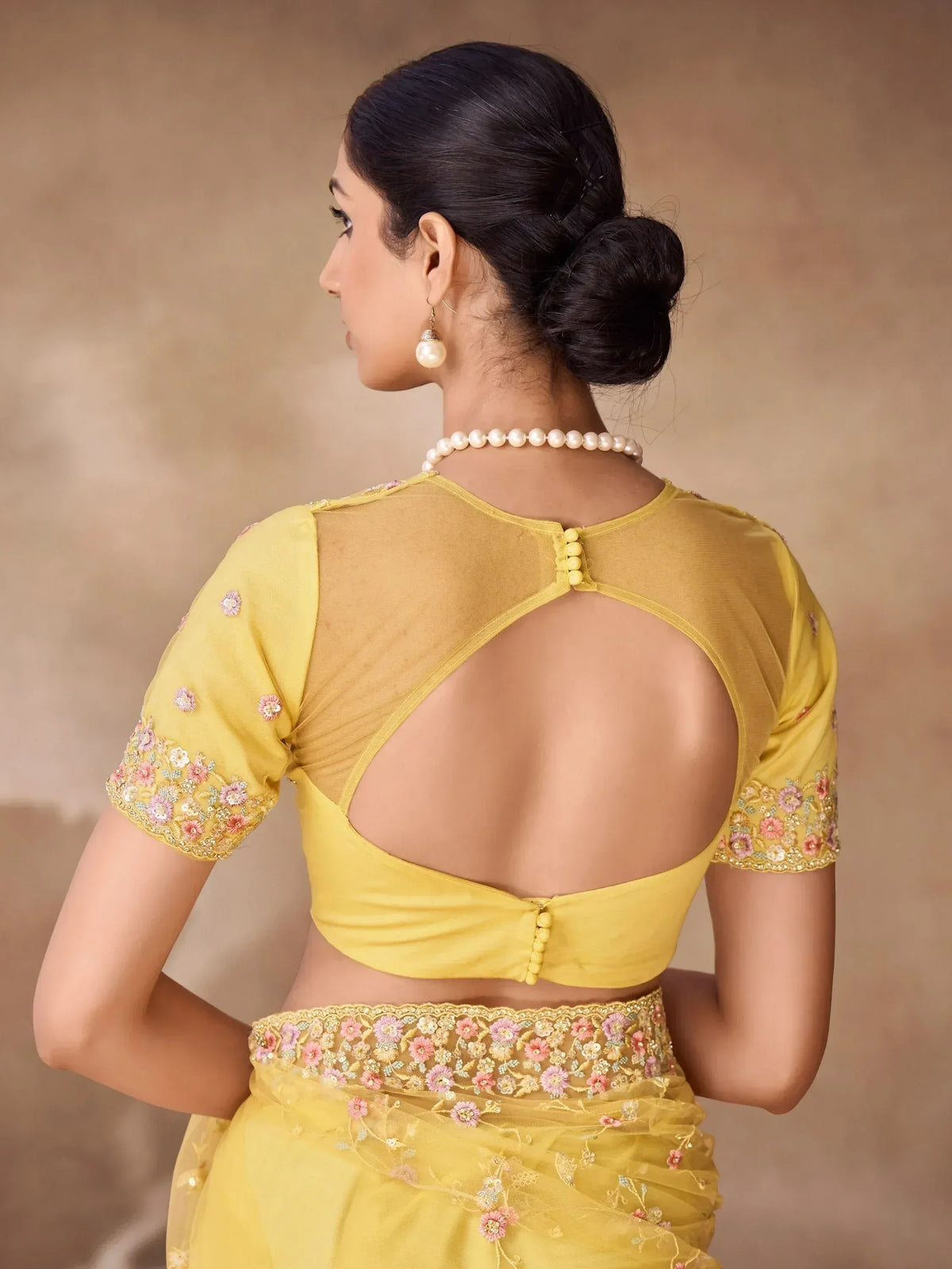 Yellow floral embroidered saree blouse with back cutout and pearl jewelry