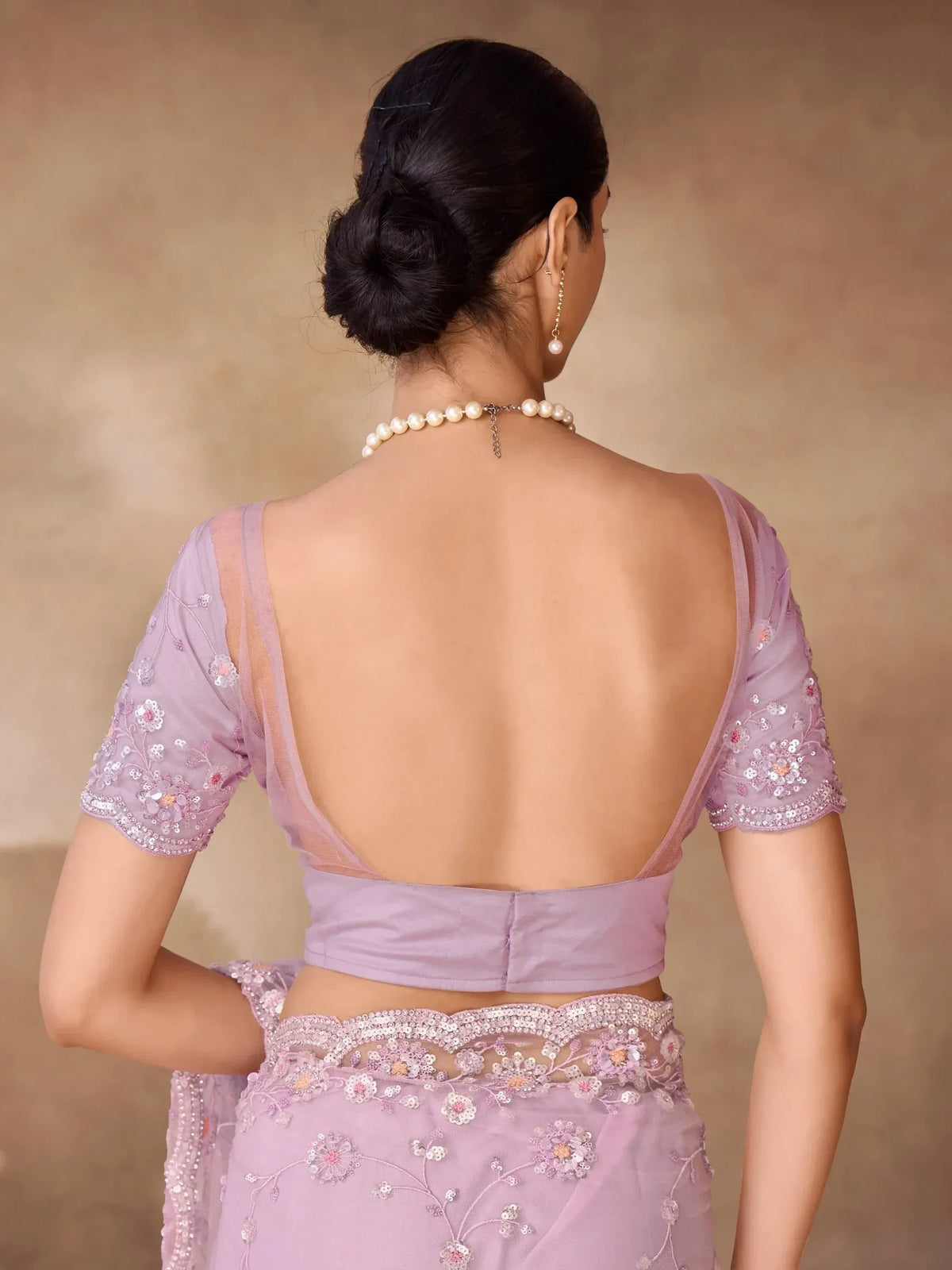 Lavender saree with floral embroidery and backless blouse, styled with pearl necklace for ethnic wear