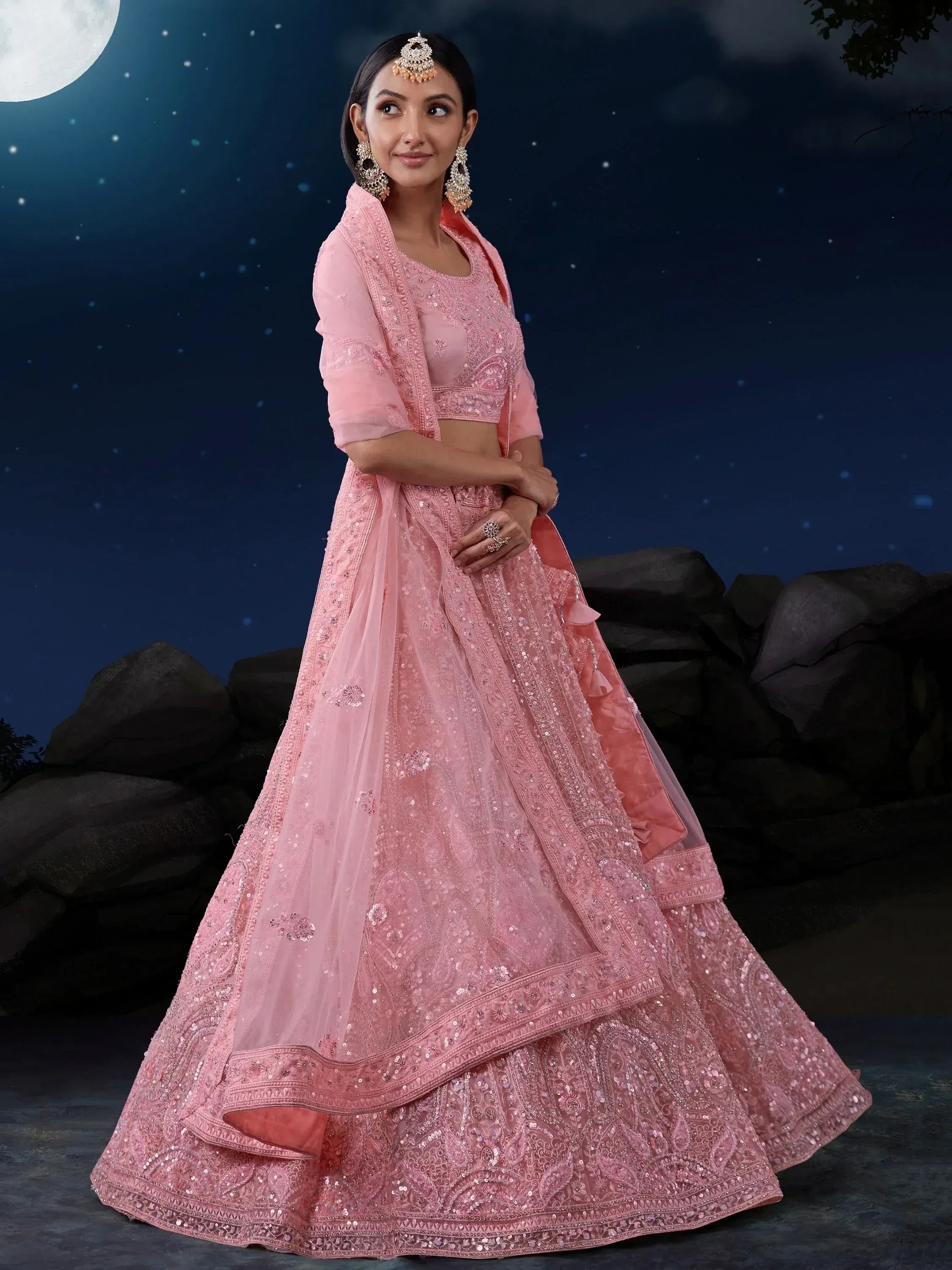 Pink designer lehenga choli with intricate embroidery, perfect for Indian weddings and festive occasions under moonlight.