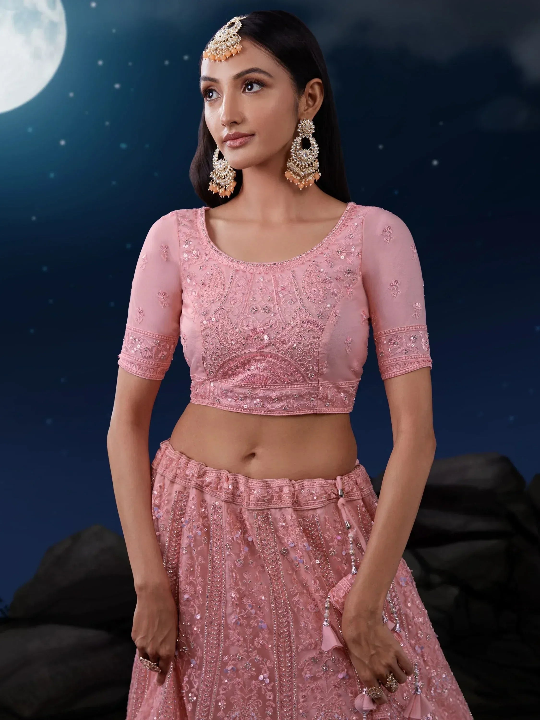 Pink embroidered lehenga choli with sequins, worn with statement jewelry under moonlit sky
