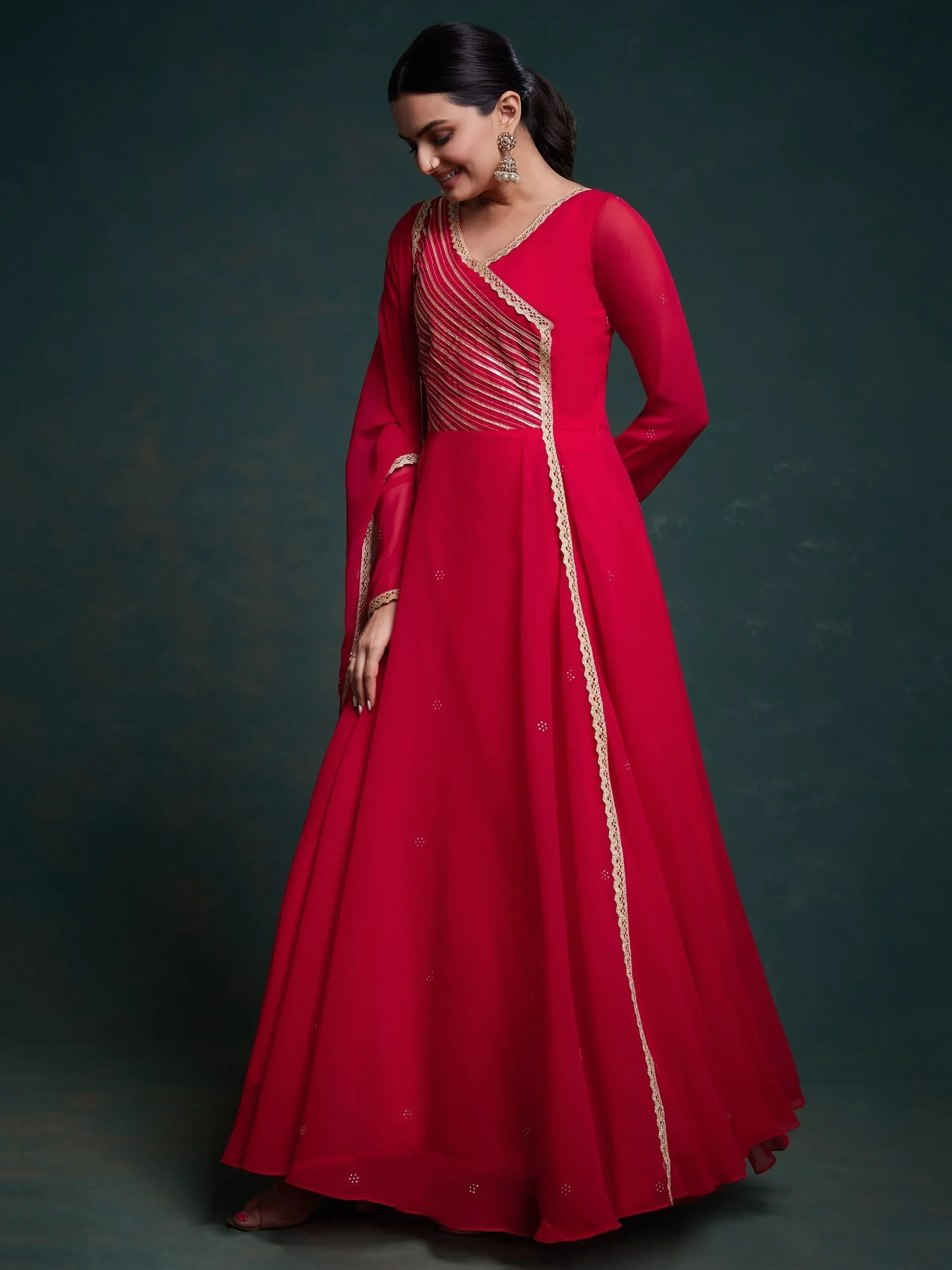 Woman in a red Anarkali gown with gold embroidery and sheer long sleeves
