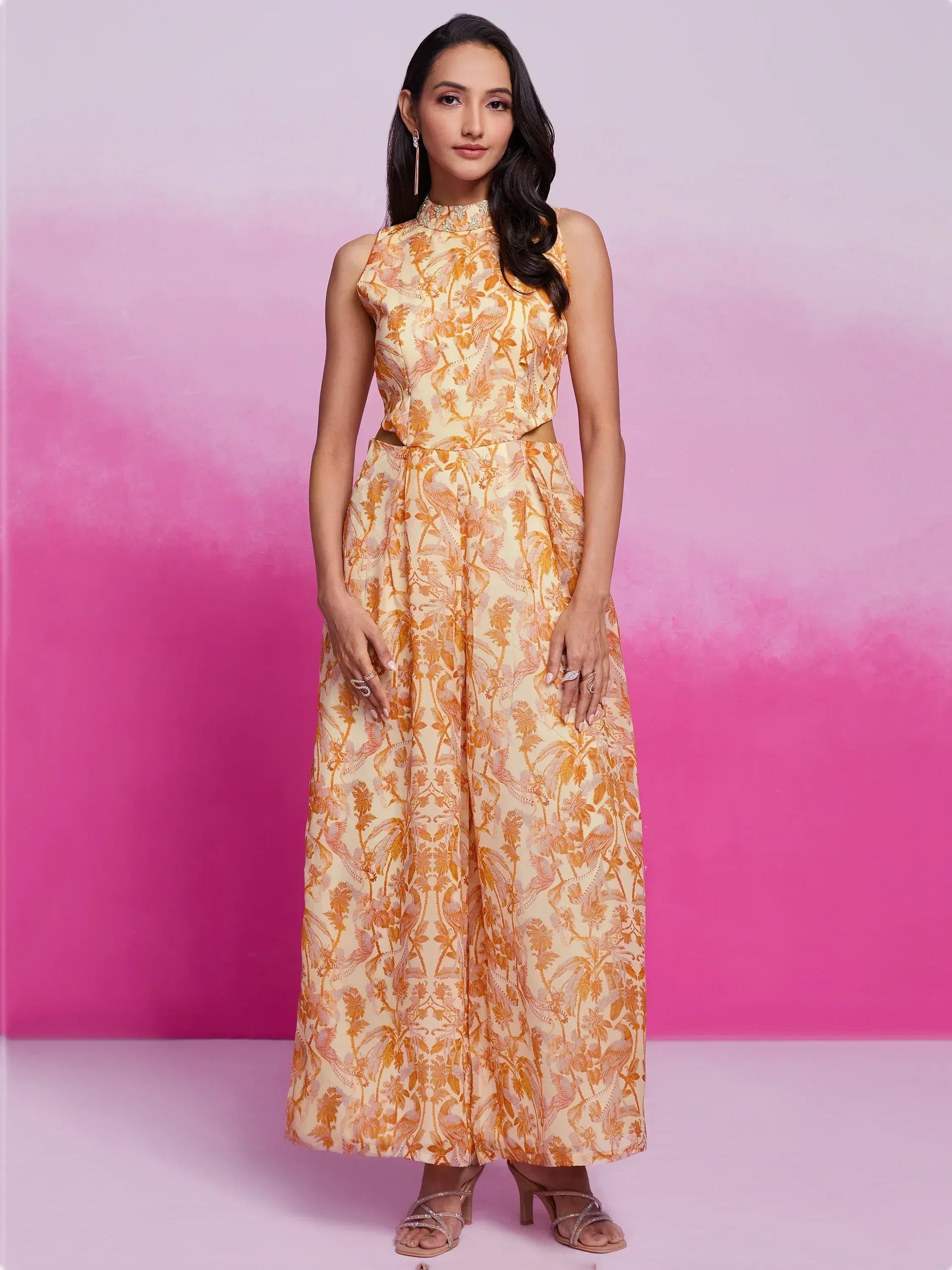 Woman in elegant orange and cream printed ethnic gown with high neck and side cutouts, perfect for festive occasions.