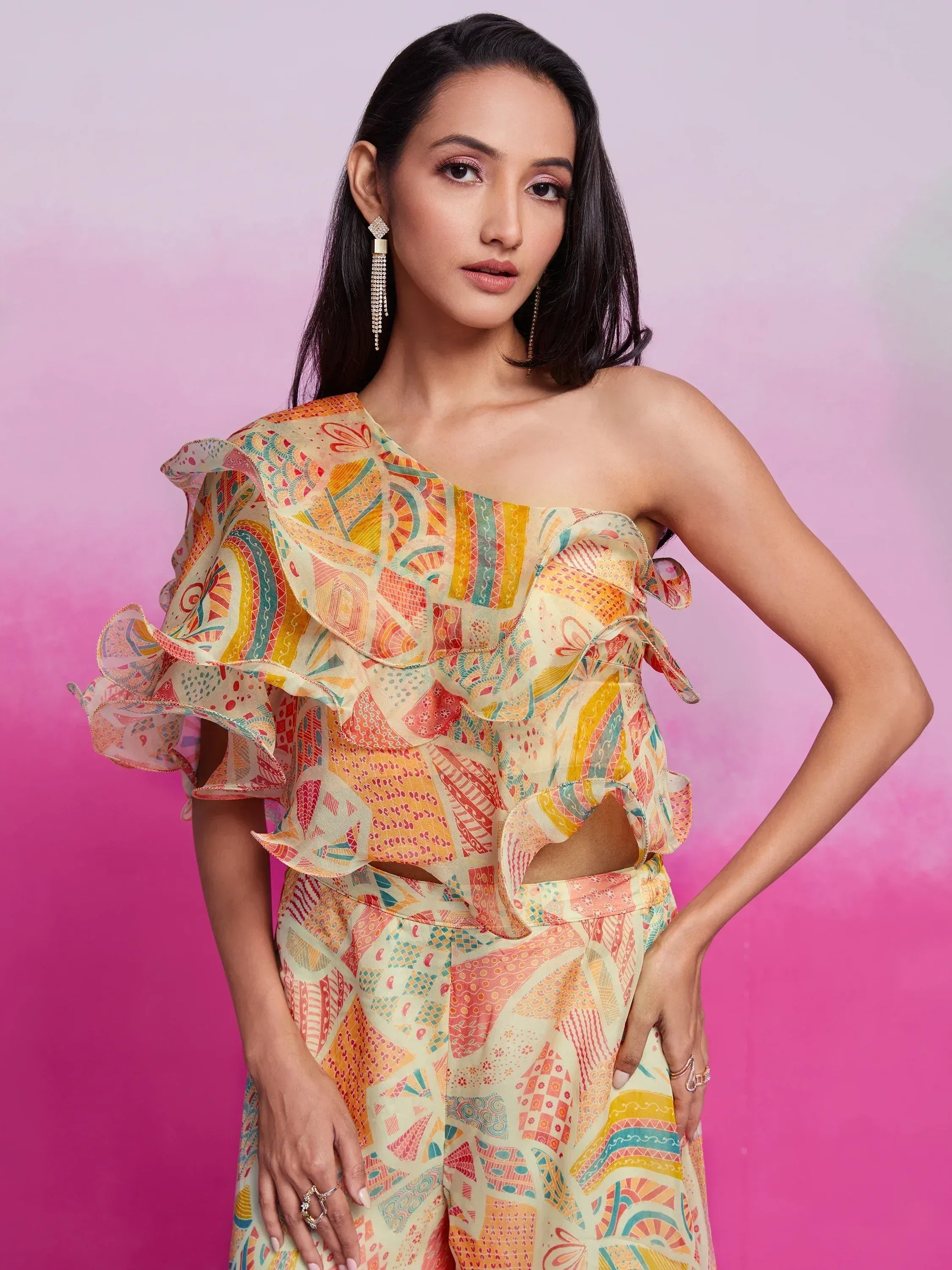 Woman wearing vibrant printed one shoulder ethnic gown with ruffle details, pink backdrop