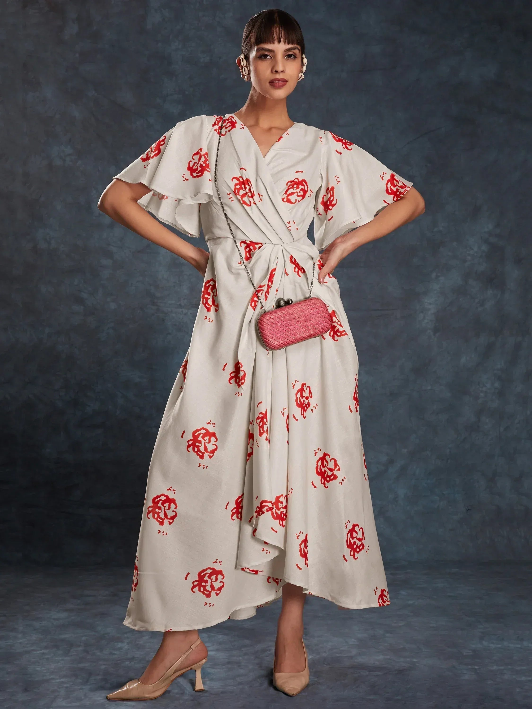 White ethnic gown with red floral print, ruffled sleeves, and wrap waist, paired with pink clutch and heels