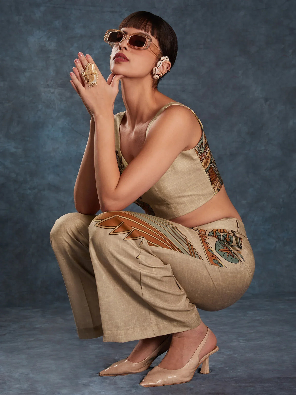 Stylish woman in beige printed ethnic crop top and palazzo pants with statement sunglasses and shell earrings