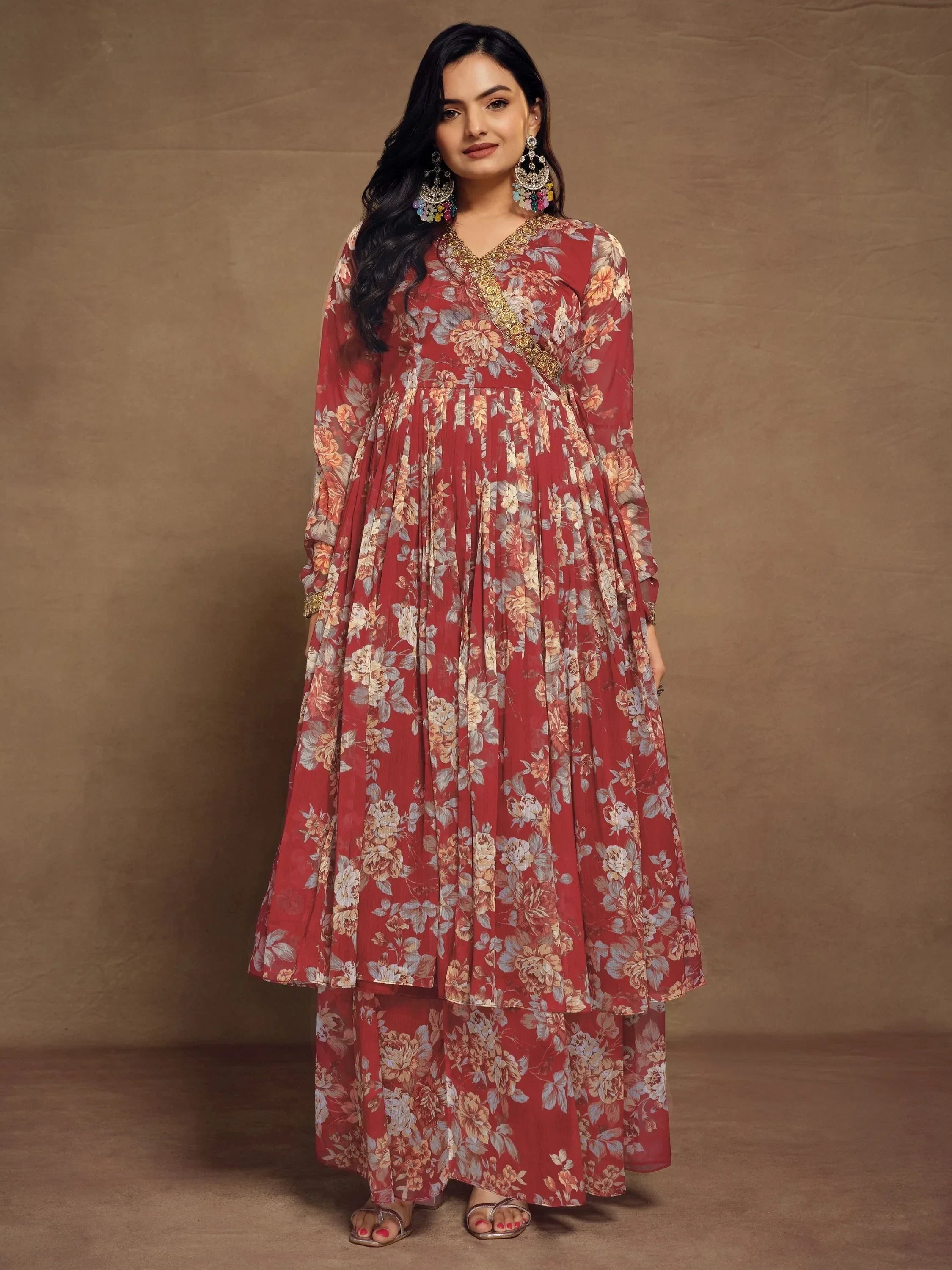 Woman in a red floral ethnic gown with long sleeves, standing against a plain background