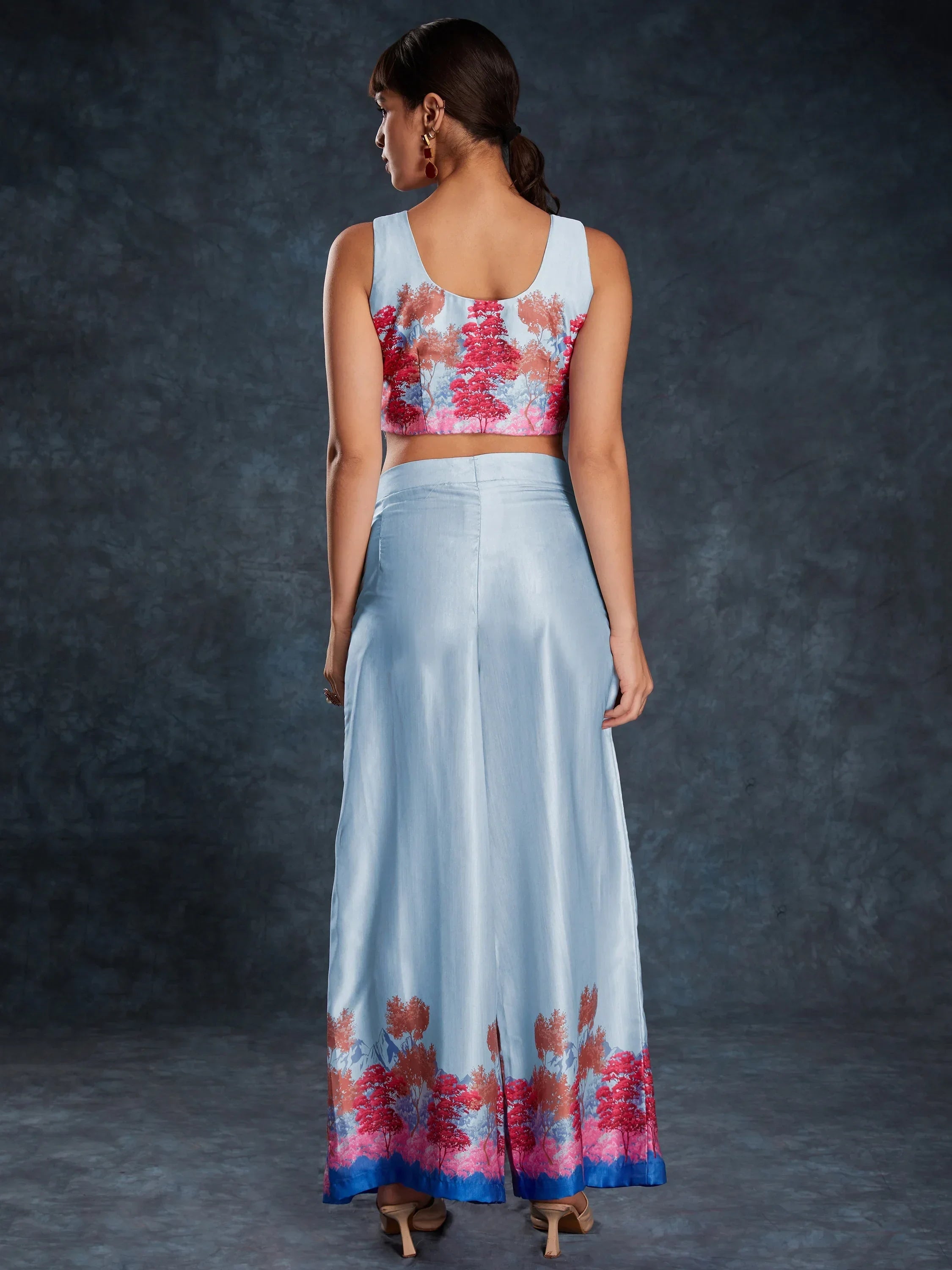 Woman in light blue ethnic crop top and wide leg palazzo with red floral print, back view