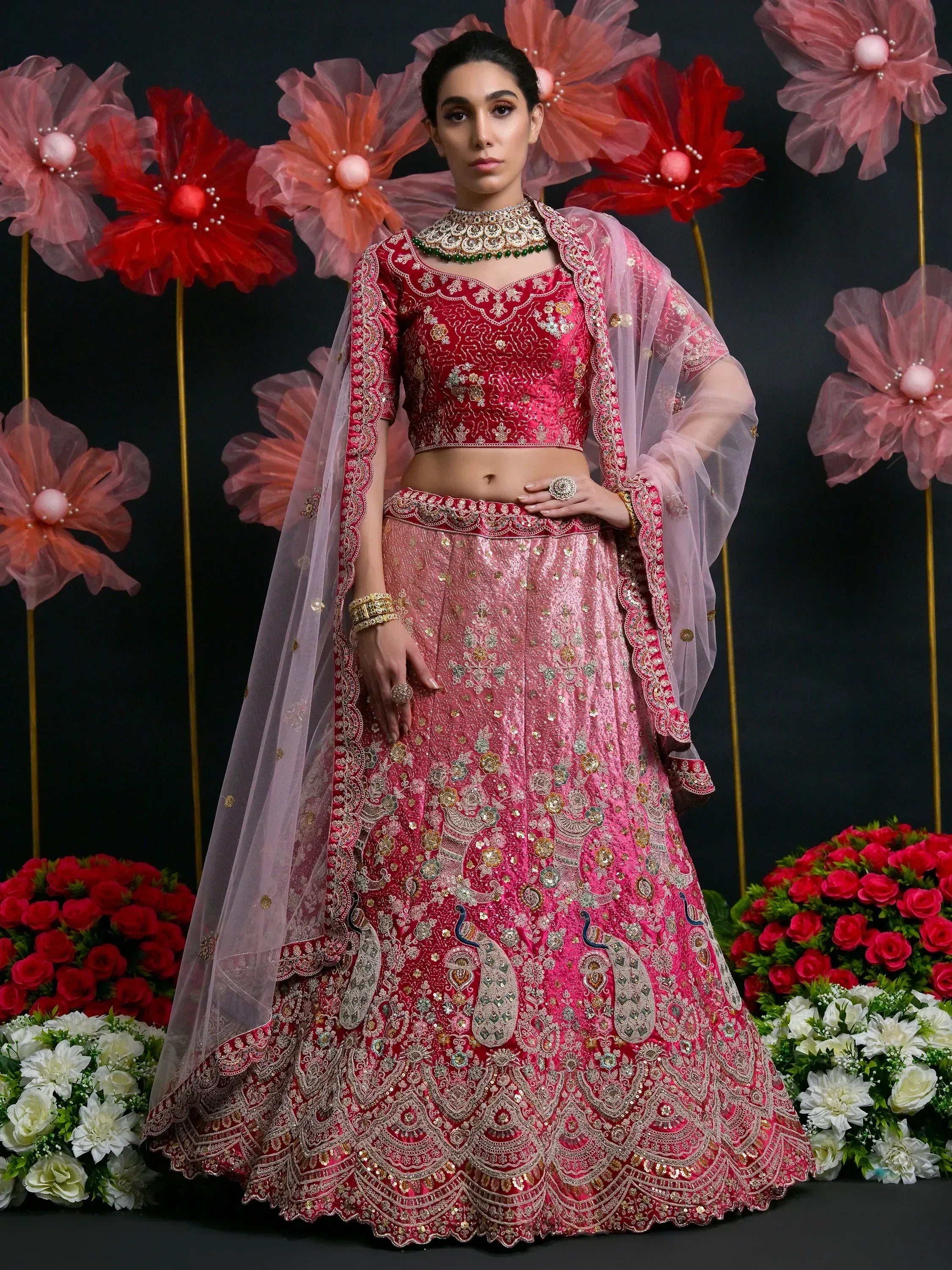 Pink and red embroidered lehenga choli with peacock motifs, sheer dupatta, and floral backdrop for Indian ethnic wear