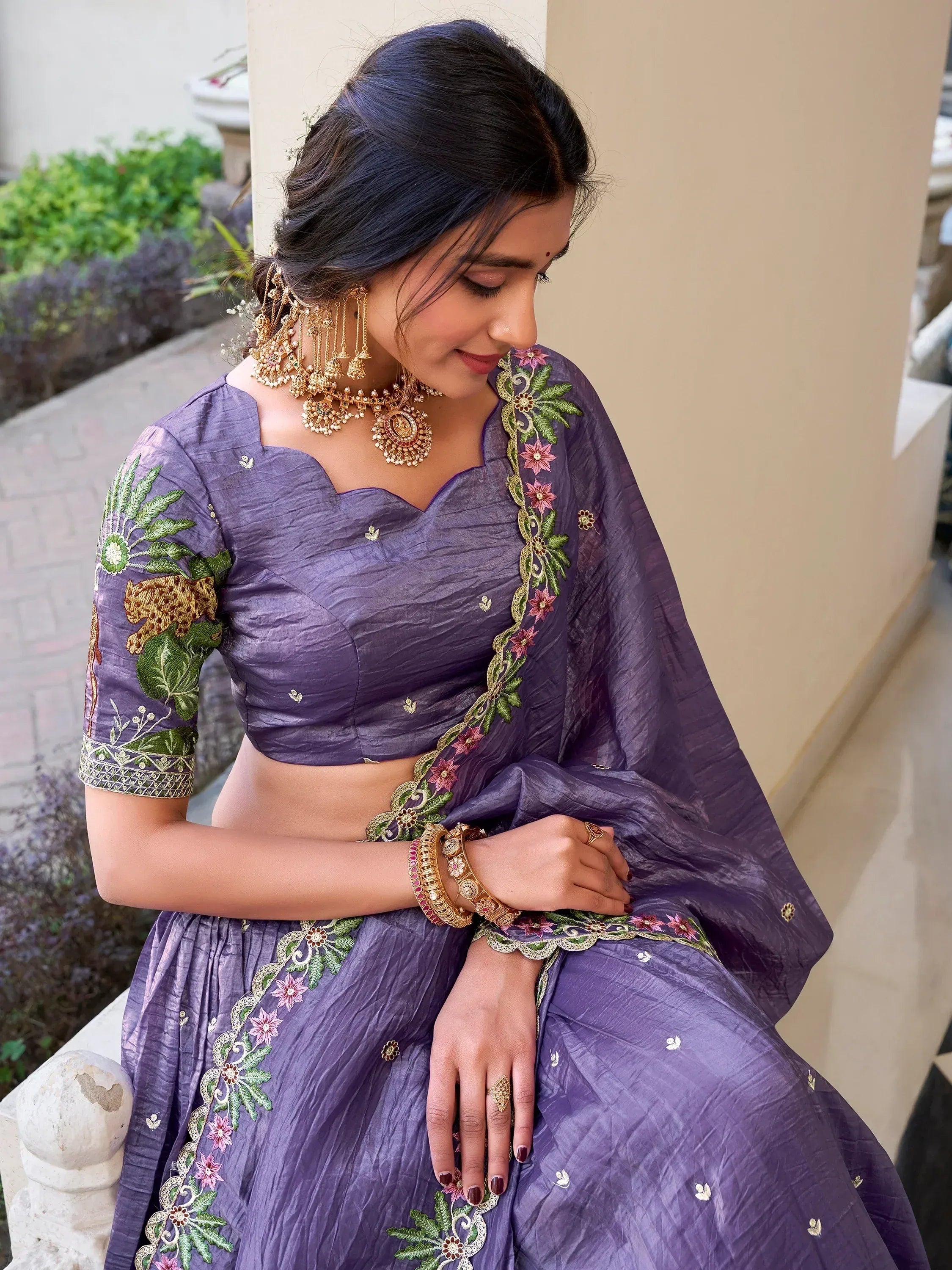 Purple embroidered lehenga choli with floral and animal motifs, paired with gold jewelry for Indian ethnic wear.