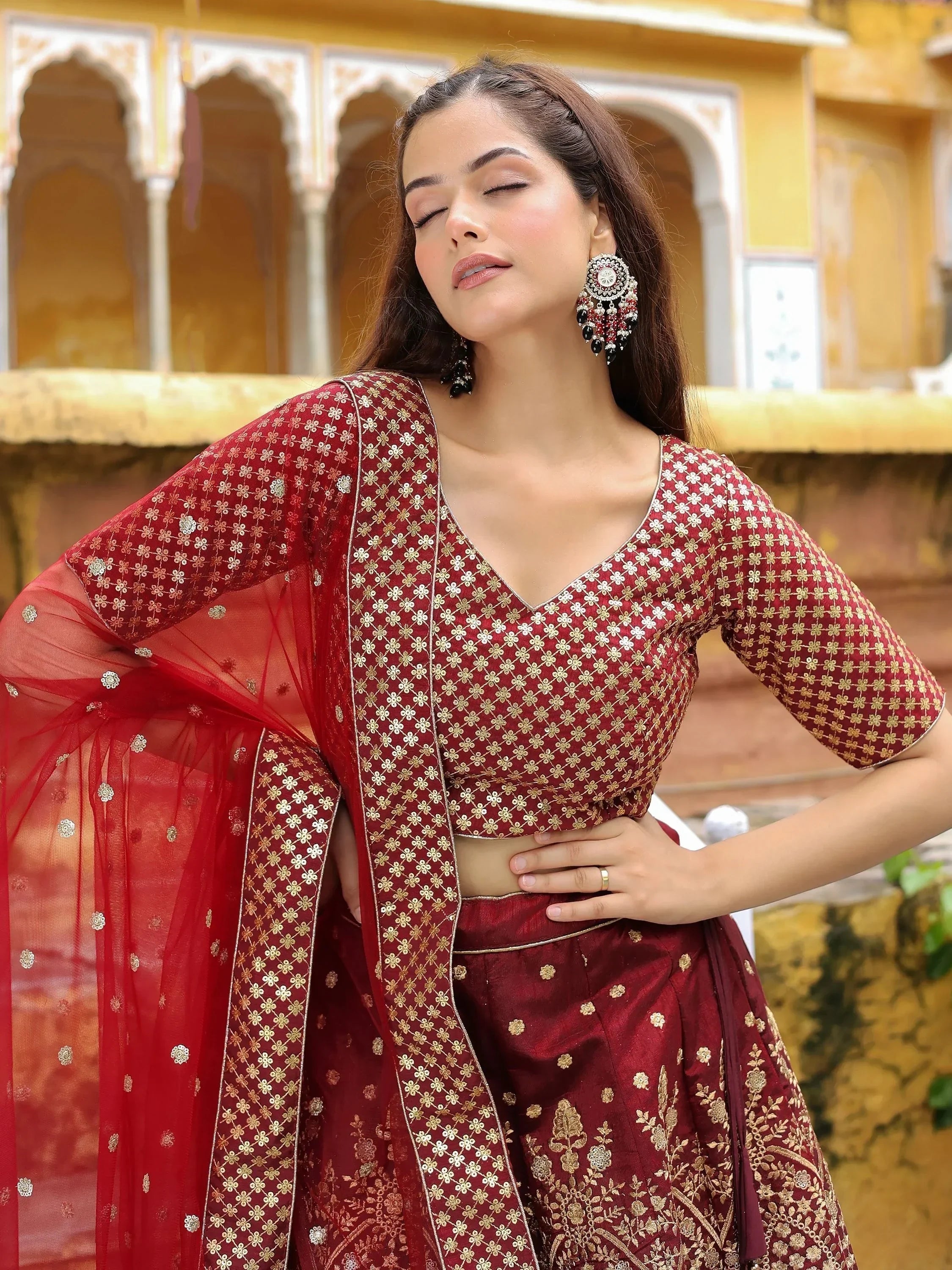 Maroon embroidered lehenga choli with gold floral motifs, sheer dupatta, and statement earrings